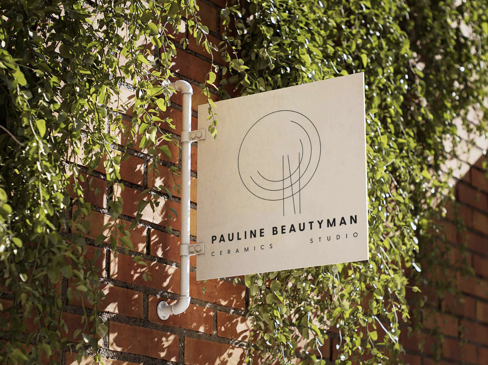 Sign for Pauline Beautyman Ceramics Studio attached to a brick wall with green climbing plants around it.