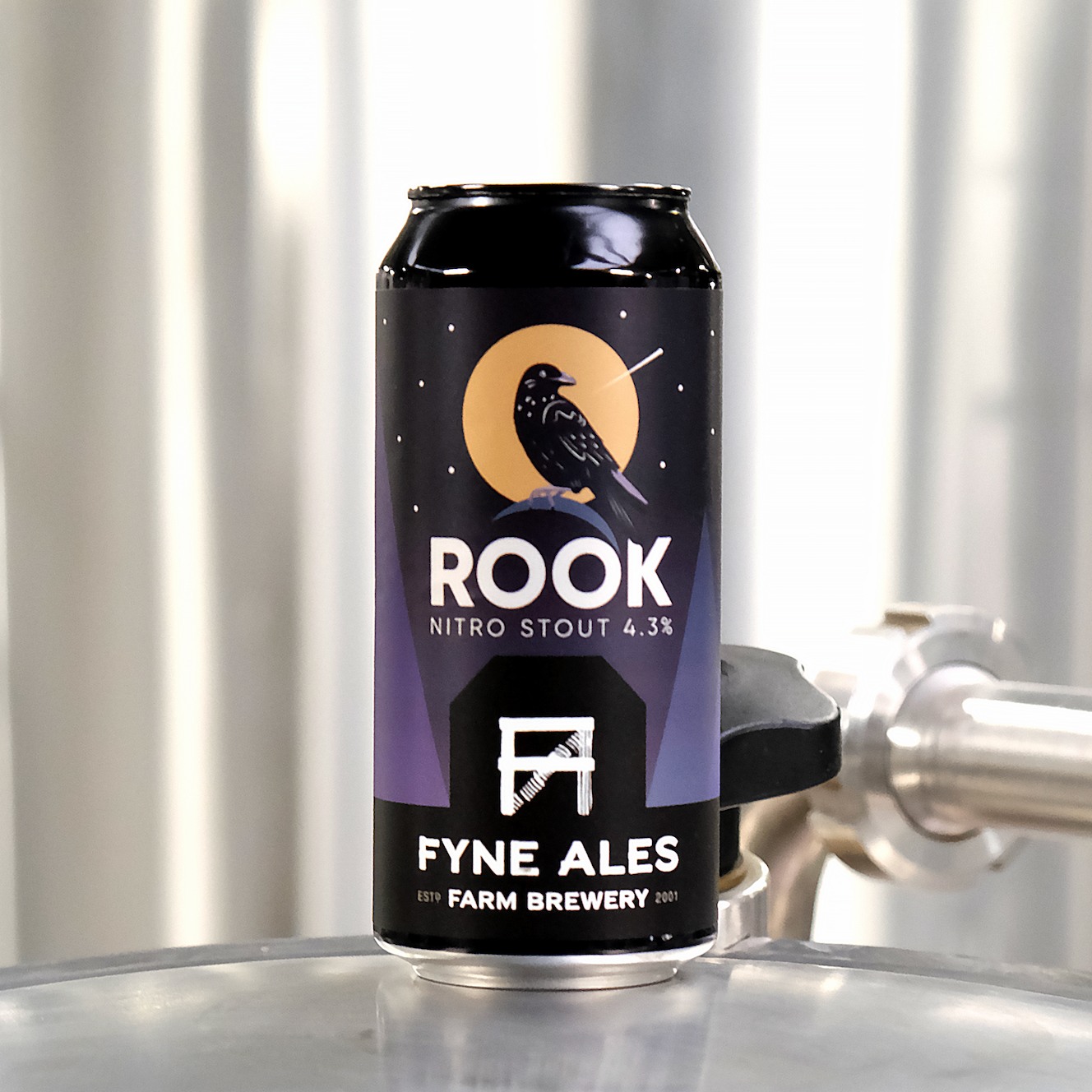 A can of Rook Nitro Stout beer with 4.3% alcohol content, featuring a black crow on a yellow moon and the logo of Fyne Ales, a farm brewery established in 2001. The can is placed on a metallic surface with a metallic cylindrical object in the backgro