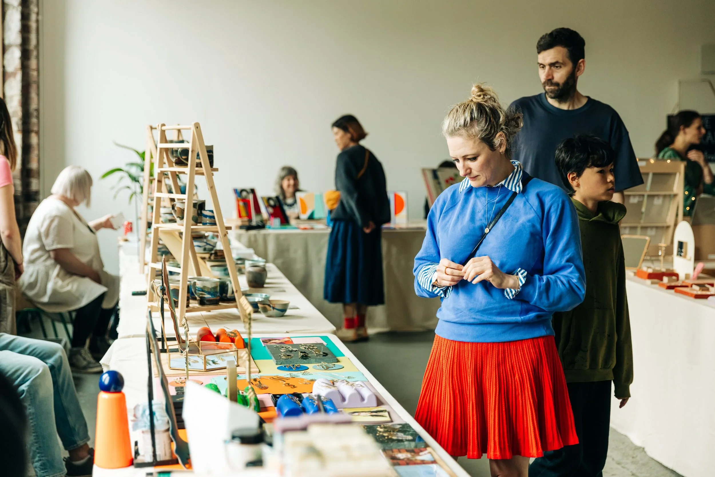People browsing handmade crafts and artwork at an indoor market or exhibition.