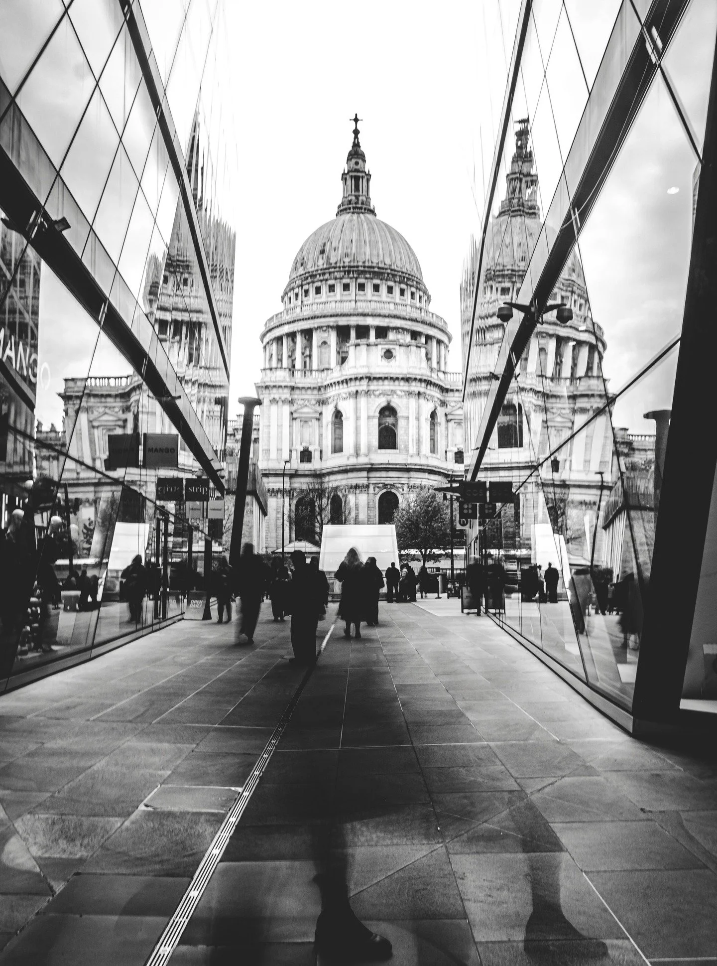 Sometimes the city feels like it&rsquo;s watching itself.
Old and new mirrored together, each trying to remember who came first.
Caught this one on a cold afternoon - people passing like shadows, the world doubling back in glass.

#streetphotography 