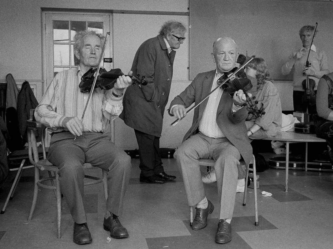 Joe Ryan and Bobby Casey playing for a fiddle class with Breandán Breathnach standing in the centre background, 1985.