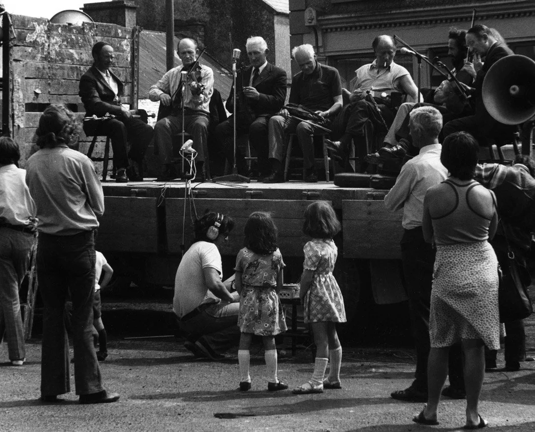 An outdoors concert in Miltown Malbay's main street with (l to r) Michael Falsey, Bobby Casey, Junior Crehan, Seán Reid, Andy Conroy, Pat Mitchell and John Kelly Senior, late 1970s.