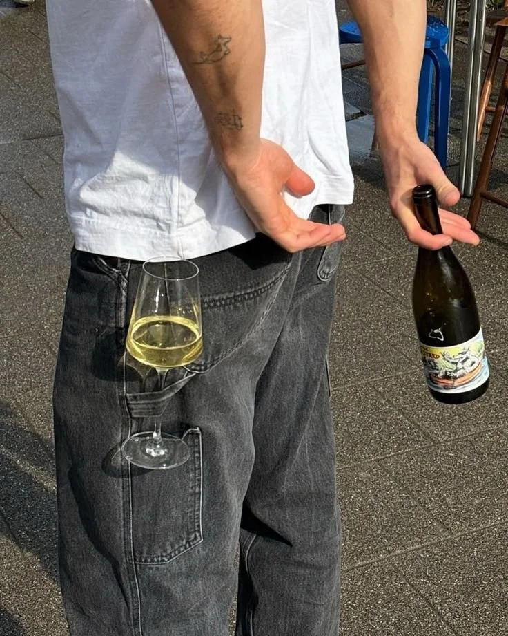Comedic bartender shot: A person holding a wine bottle in one hand and a wine glass with white wine hung in their cargo hammer pocket.