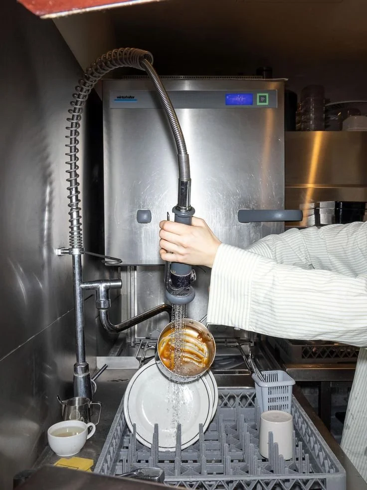A person in a white striped shirt is washing dishes as a Porter in a commercial kitchen.