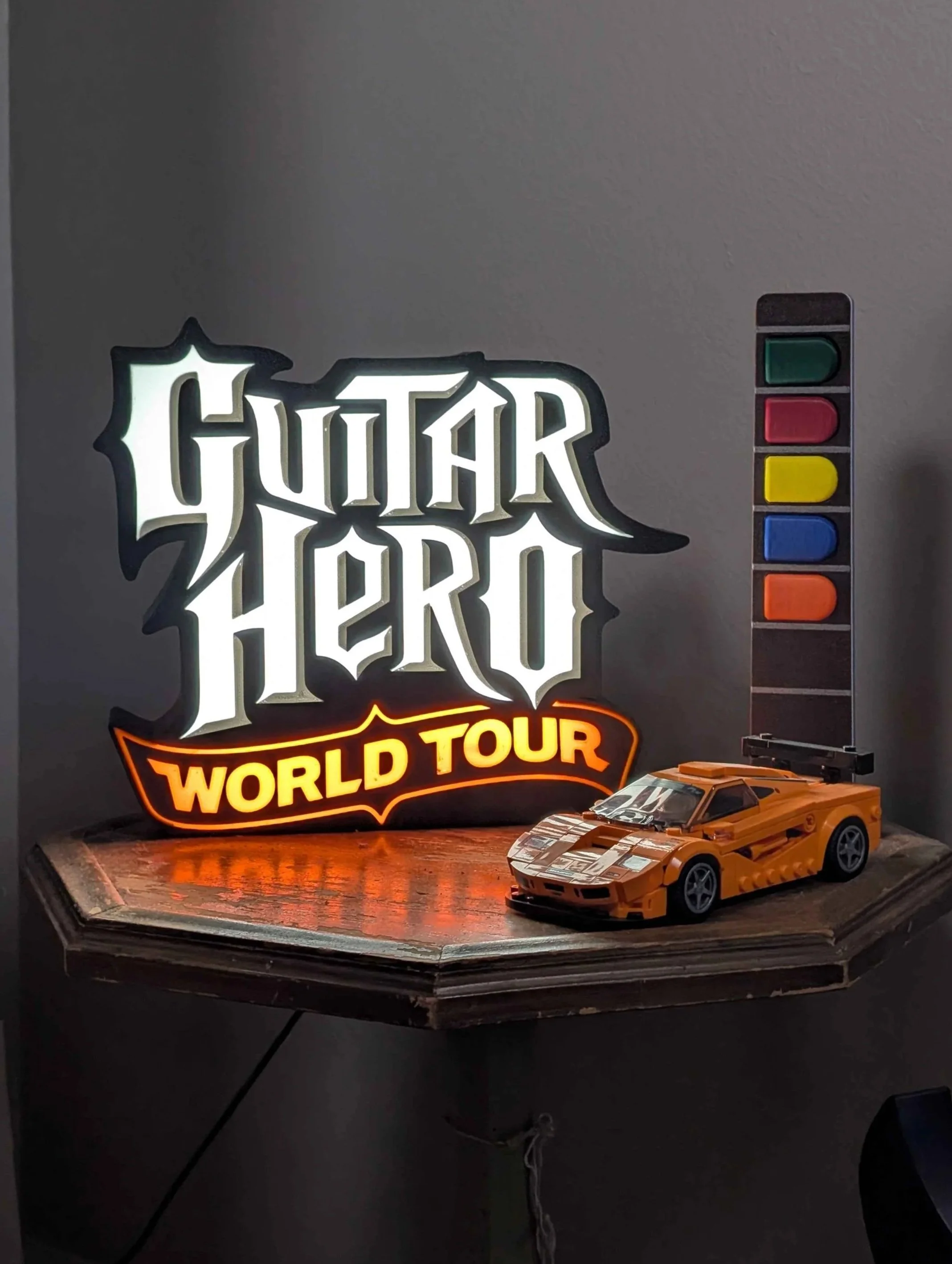 Light box on small table displaying Guitar Hero World Tour Logo next to small Lego car