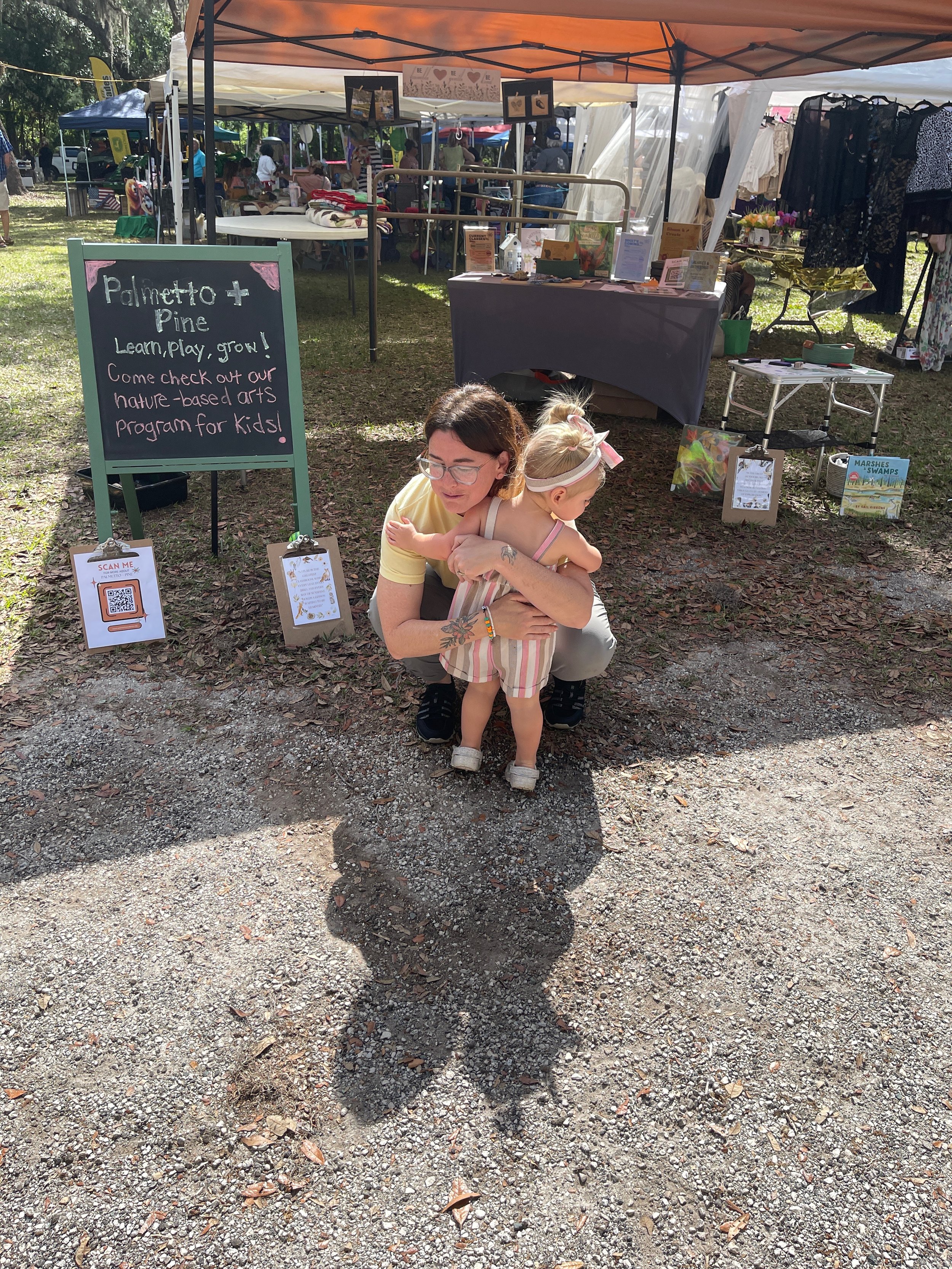 A toddler embraces her nature school teacher in a hug at a farmer's market
