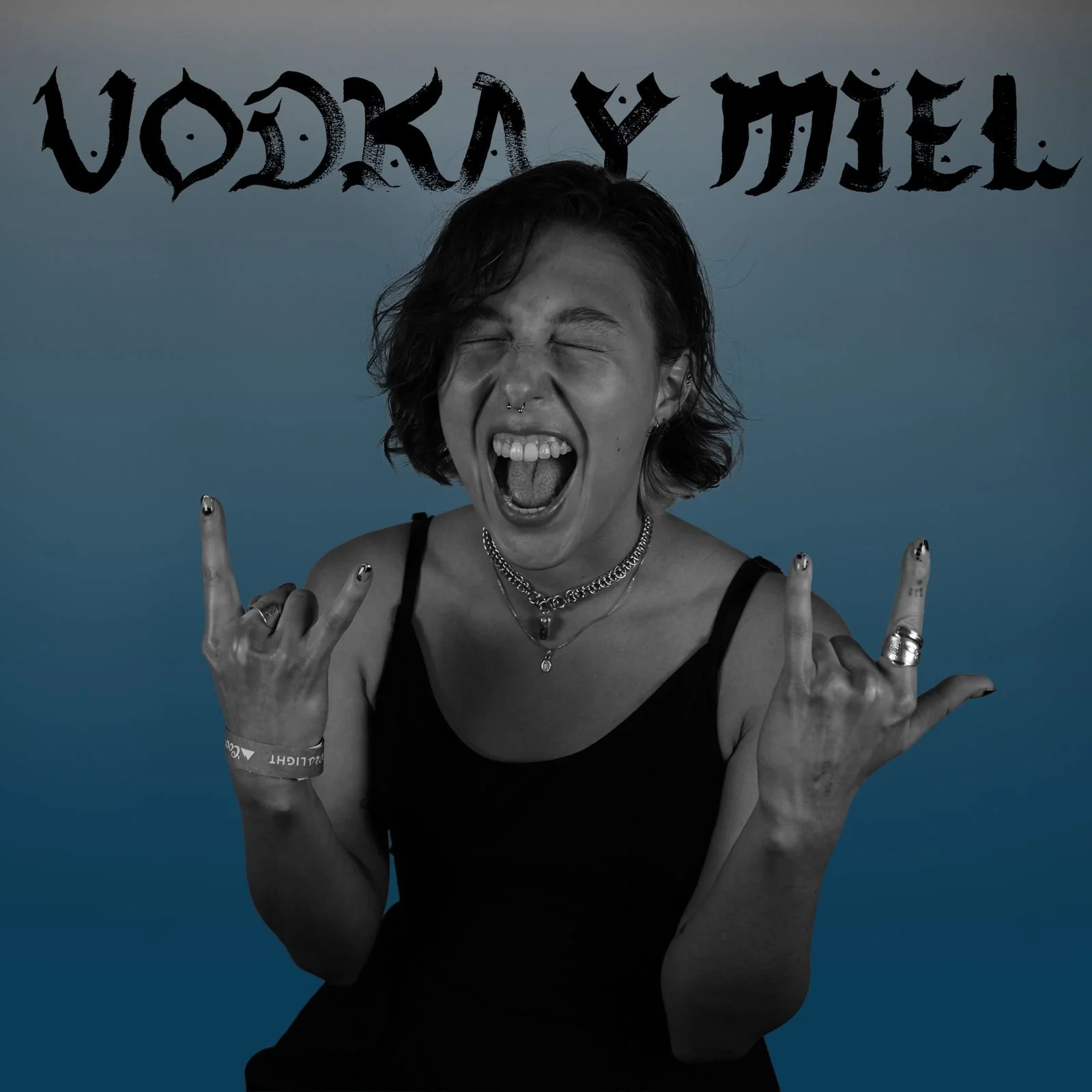 A woman with short dark hair, wearing a black tank top, making a rock sign with both hands, her tongue out, eyes closed, and mouth wide open, with the word 'WOODKAY' in stylized text above her head.