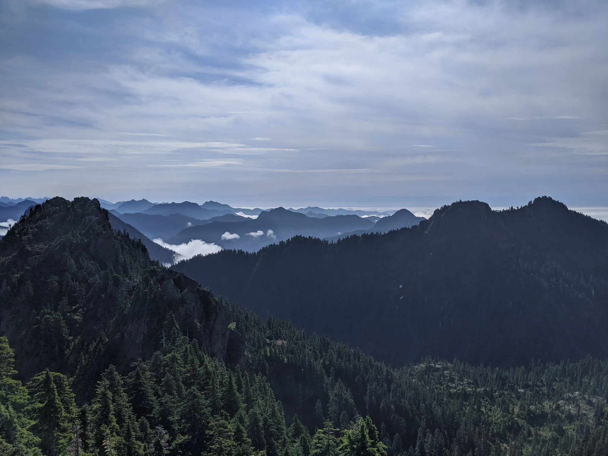 Mountain landscape with forested peaks and valleys under a cloudy sky.