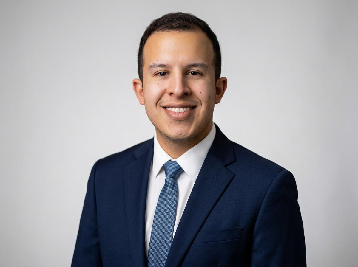 Professional portrait of a smiling man in a navy suit, white shirt, and blue tie, against a plain light gray background.