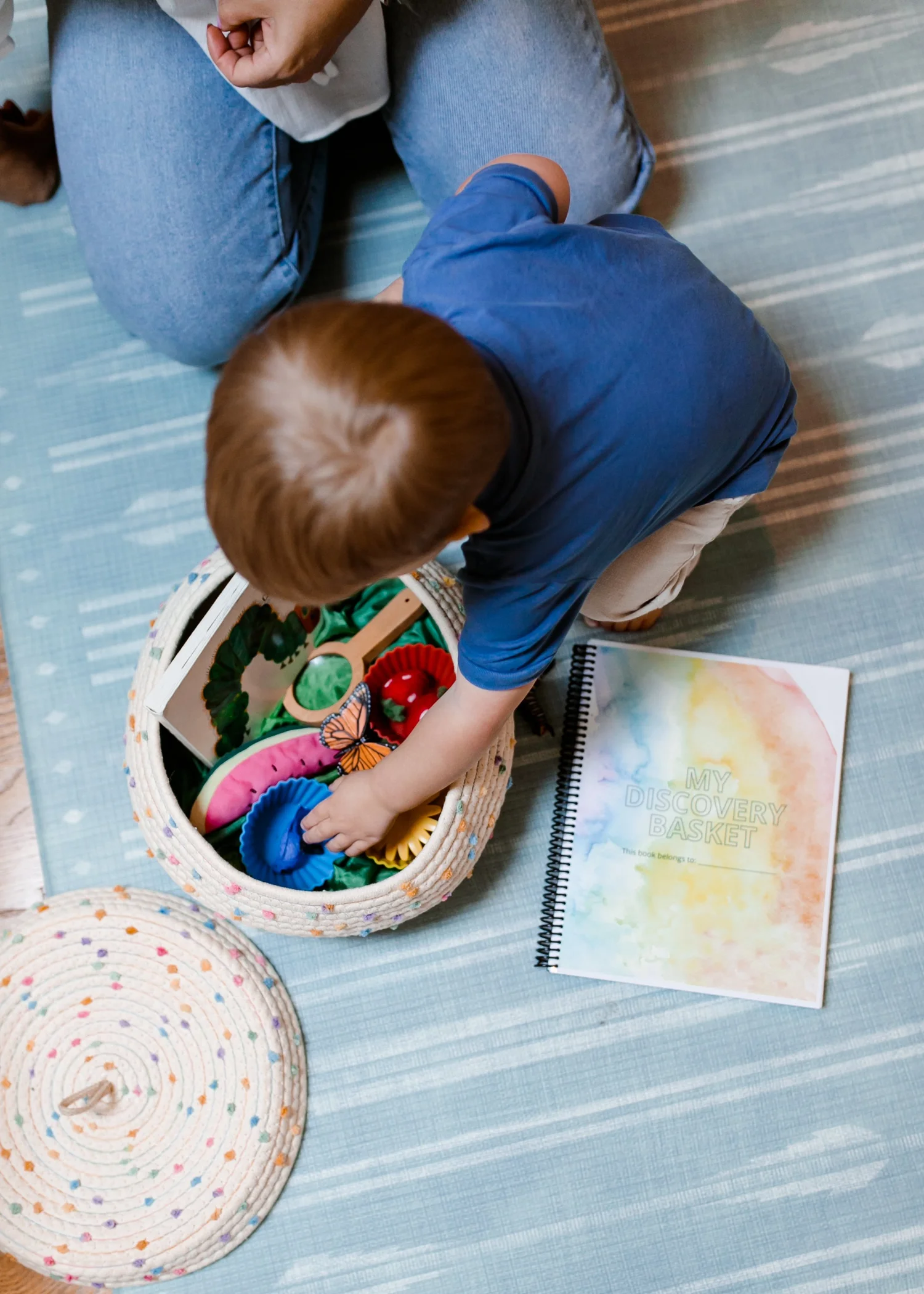 Fifteen-month-old toddler exploring a woven basket of fabric pieces on the floor