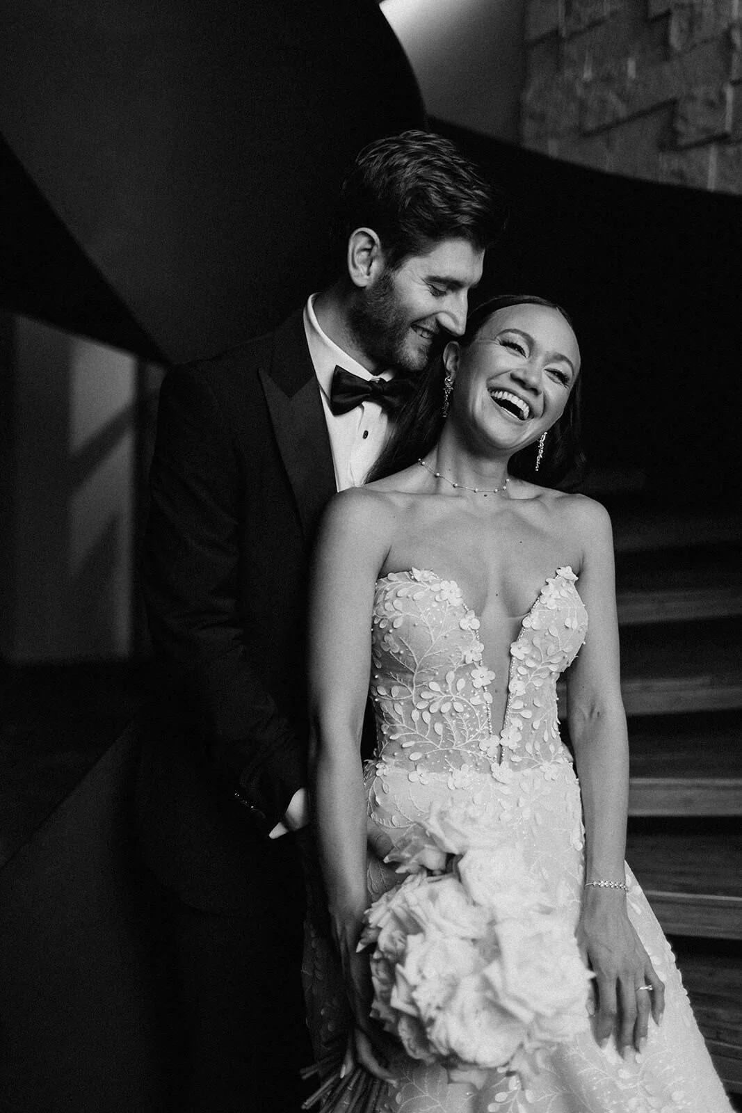 Black and white portrait of a laughing bride and groom on the staircase at Secrets Moxché Playa del Carmen