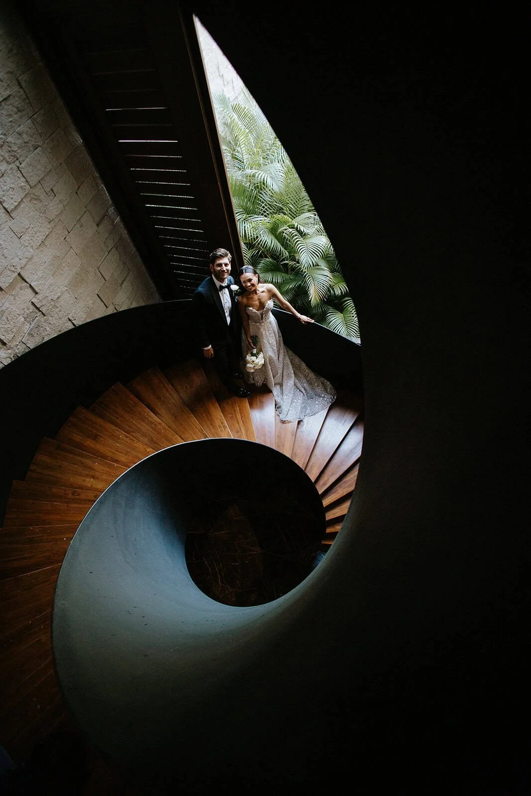 Bride and groom on the spiral wooden staircase at Secrets Moxché Playa del Carmen, tropical ferns visible through the window