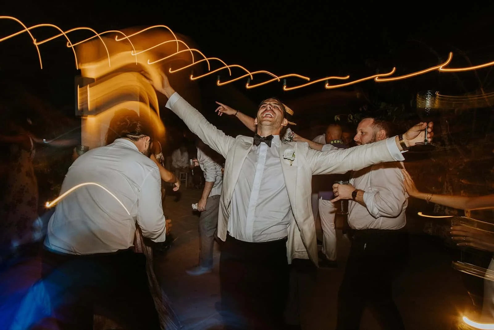 Groom Celebrates with Arms Raised Under Light Installation