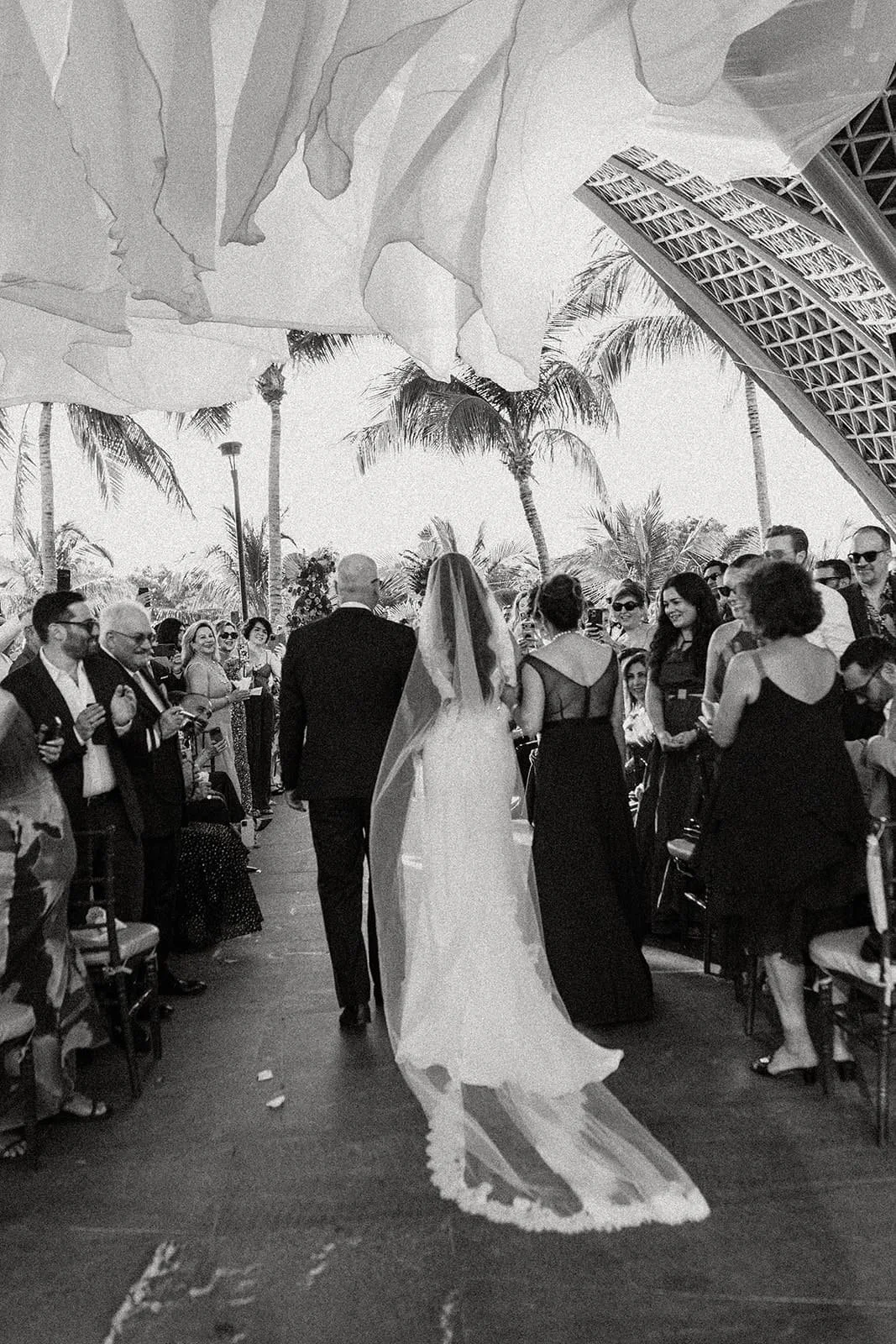 Bride walking down the aisle with father under flowing fabric canopy at Persian wedding at Garza Blanca Cancún