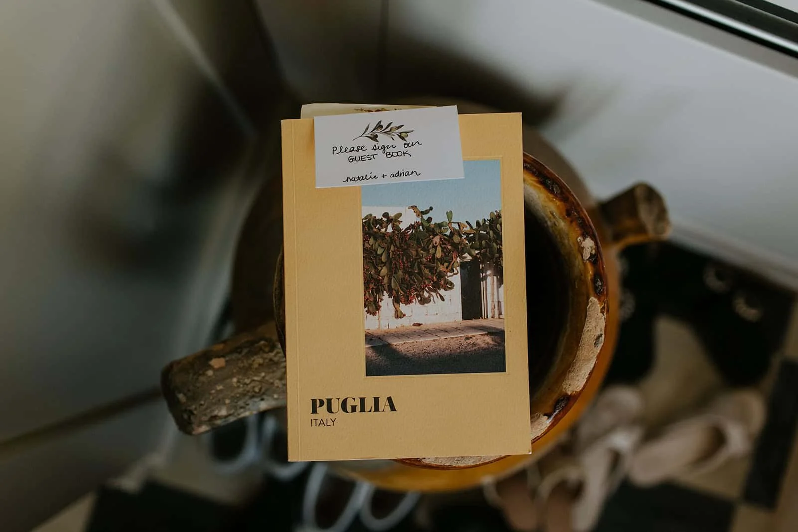 Tan colored guest book booklet labeled "PUGLIA ITALY" with dried pepper photograph, placed on wooden surface