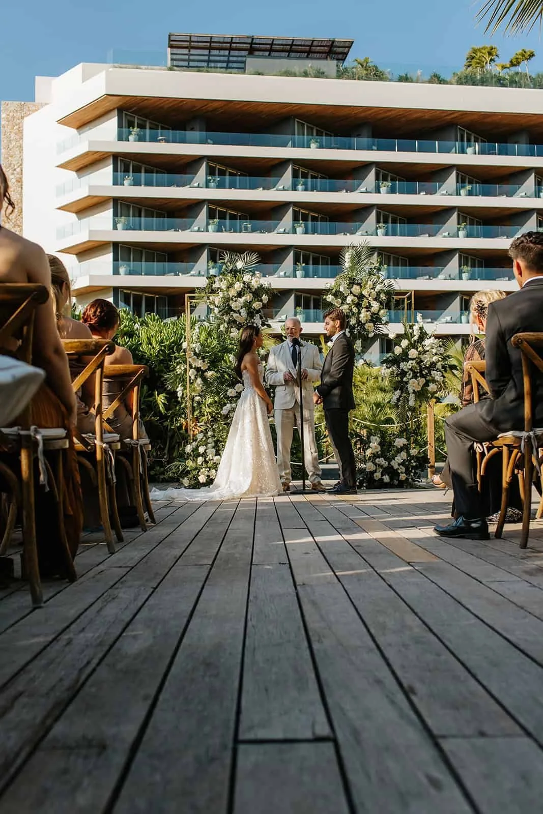 Wedding ceremony on the Pool Deck at Secrets Moxché Playa del Carmen, couple at a floral arch with the resort tower rising behind them