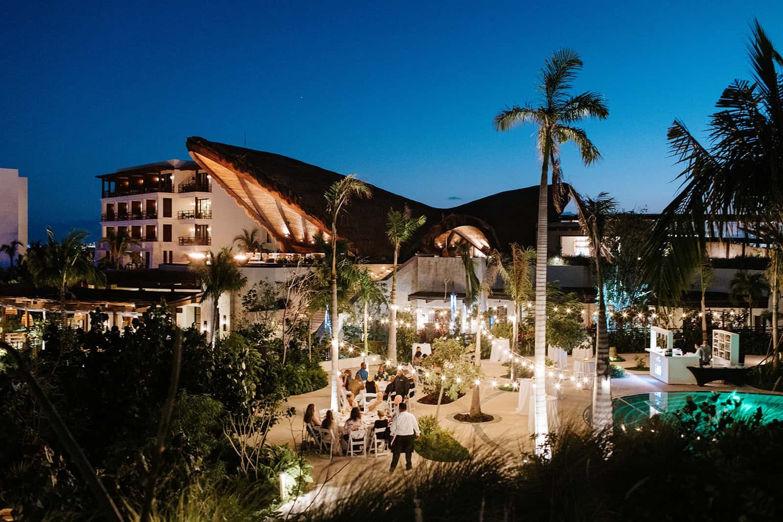 Wedding welcome dinner with the palapa-roofed lobby lit up in the background at Secrets Playa Blanca Costa Mujeres