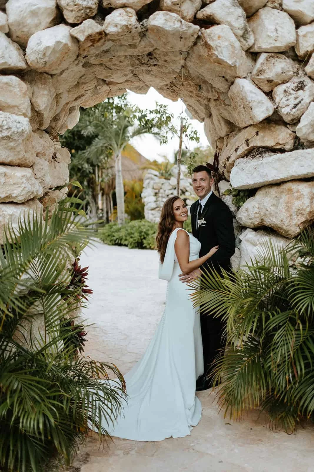 Bride and groom portrait framed by a stone archway with tropical planting at Secrets Moxché Playa del Carmen