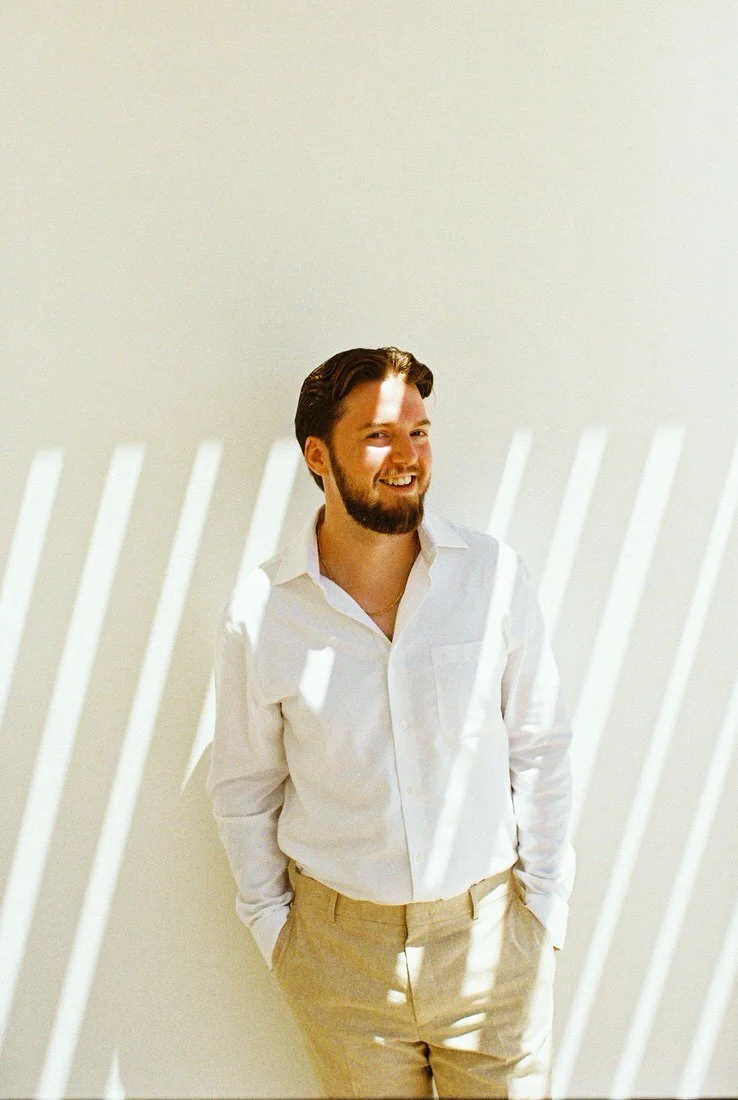Groom standing against a sunlit wall with shadow patterns, photographed on film in Cancun, Mexico.