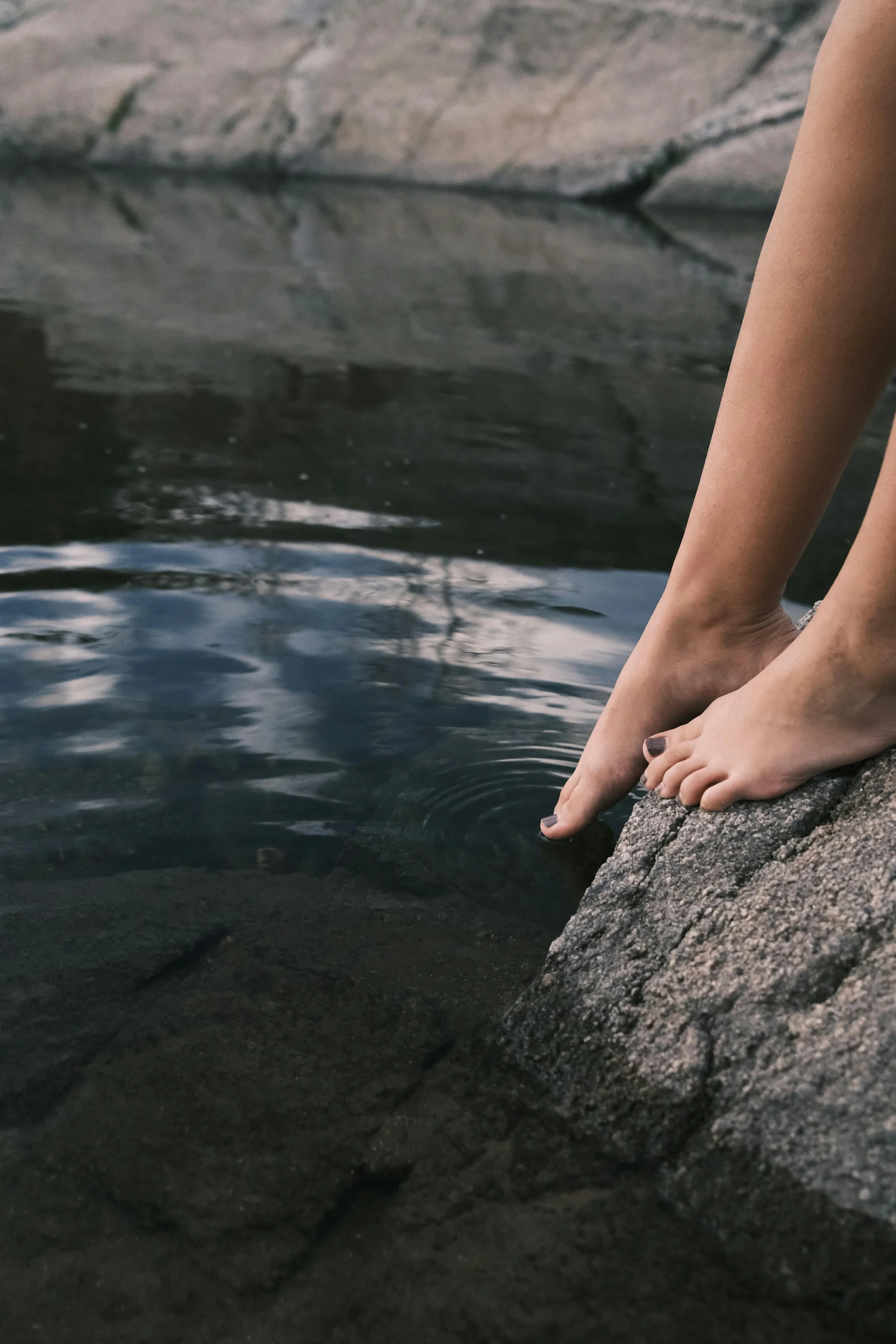 Person with painted nails touching water near rocks.