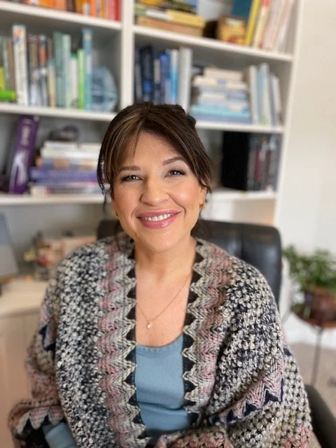 Holly Tofanelli with Resonate Therapy and Wellness is sitting in a patterned shawl sitting in front of a bookshelf filled with books.
