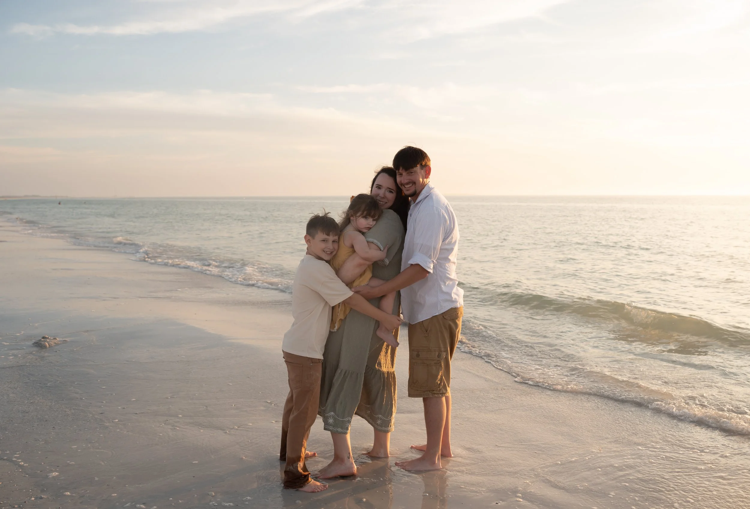 Black and white photo of a smiling family outdoors, with two adults and two children, dressed in casual fall clothing.