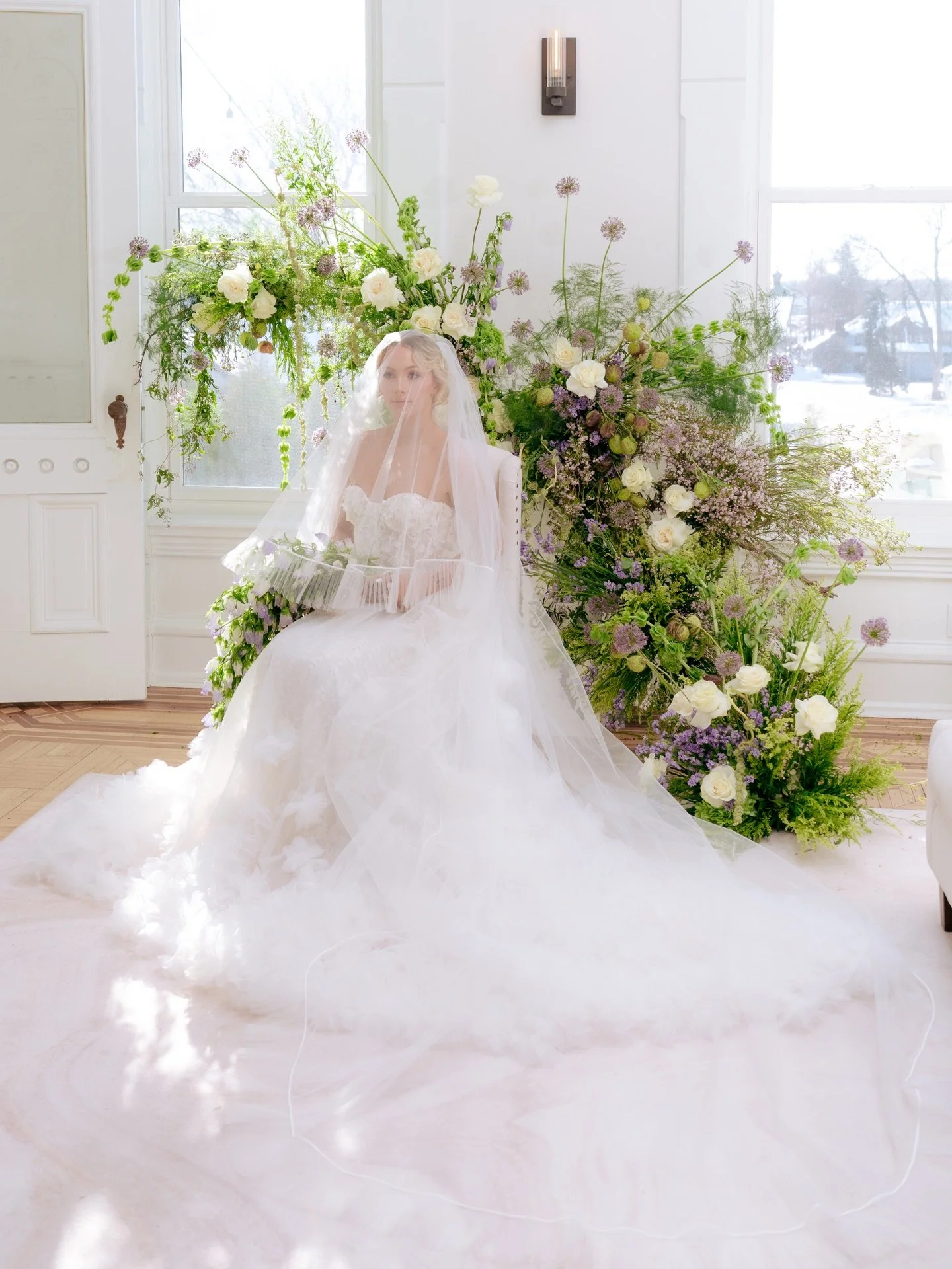 Soft light spills across antique parquet floors as a veil catches the air, florals stretching toward the windows as though the room itself has decided to bloom. This editorial was an ode to silliness and quiet strength - layers of ivory tulle softene