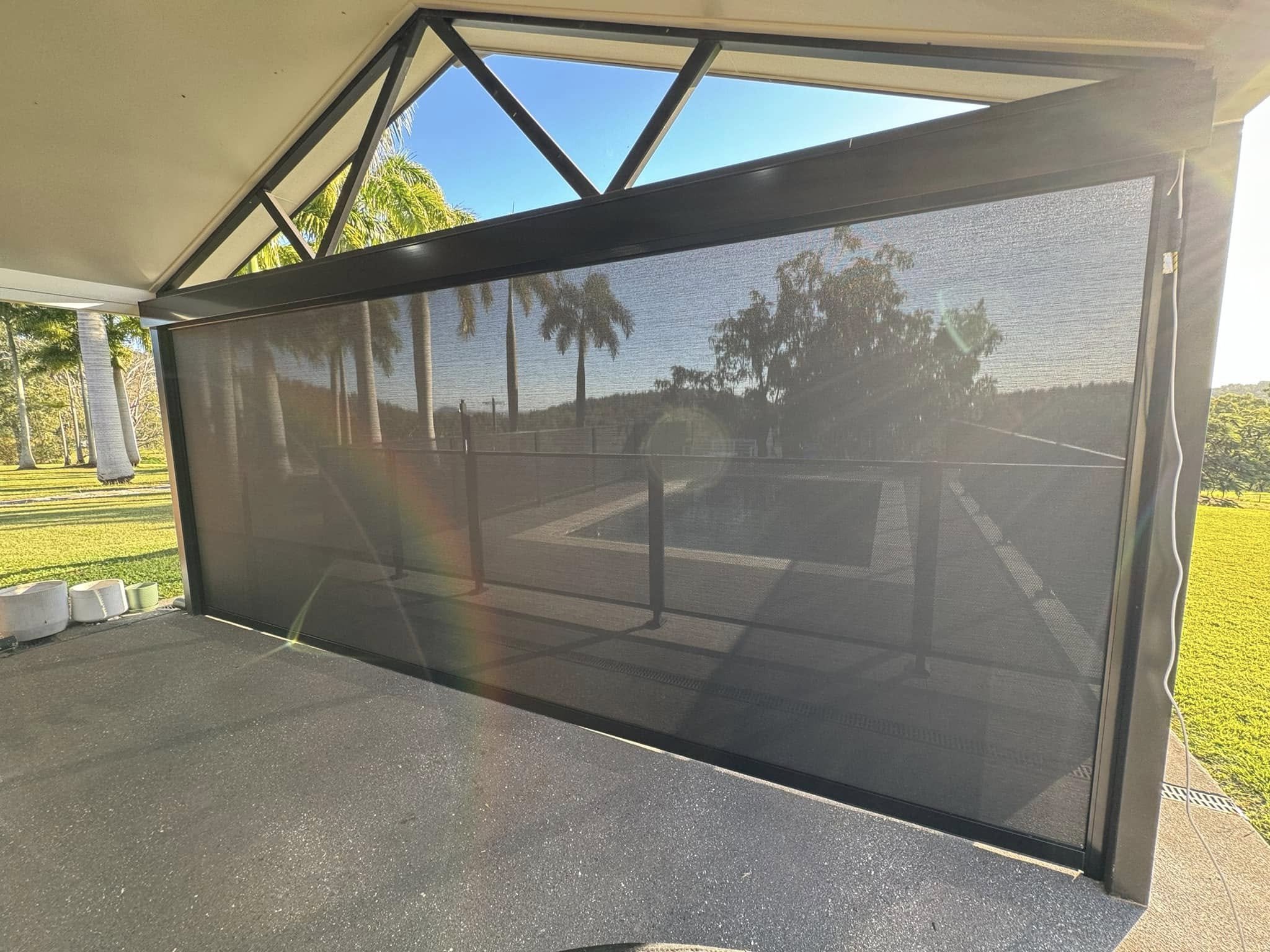 External view of a house with a zipscreen blind blocking the sun. Grey concrete driveway, white pitched roof, blue sky and green grass