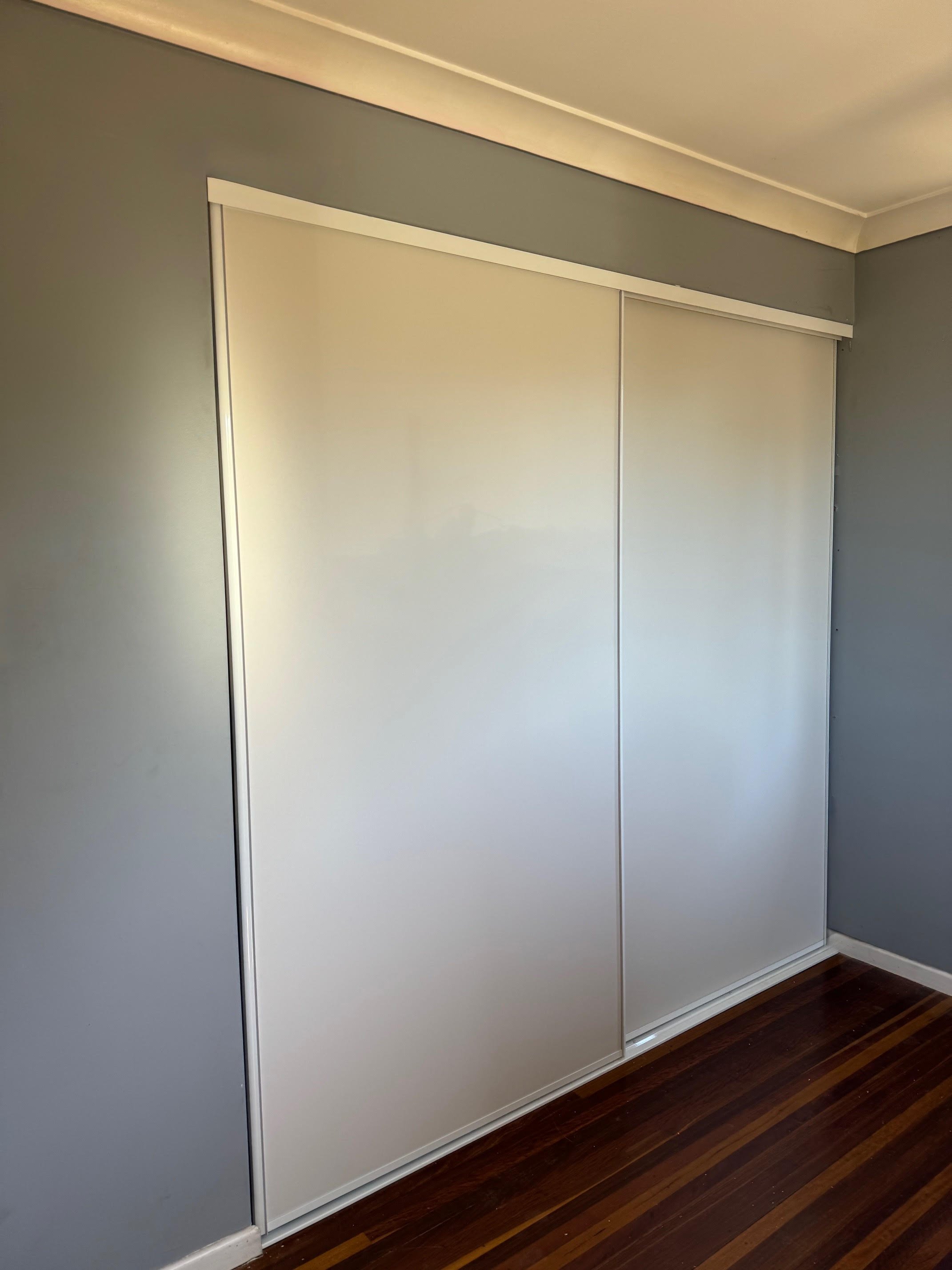 White vinyl sliding wardrobe doors in a bedroom with grey walls and dark wooden floor