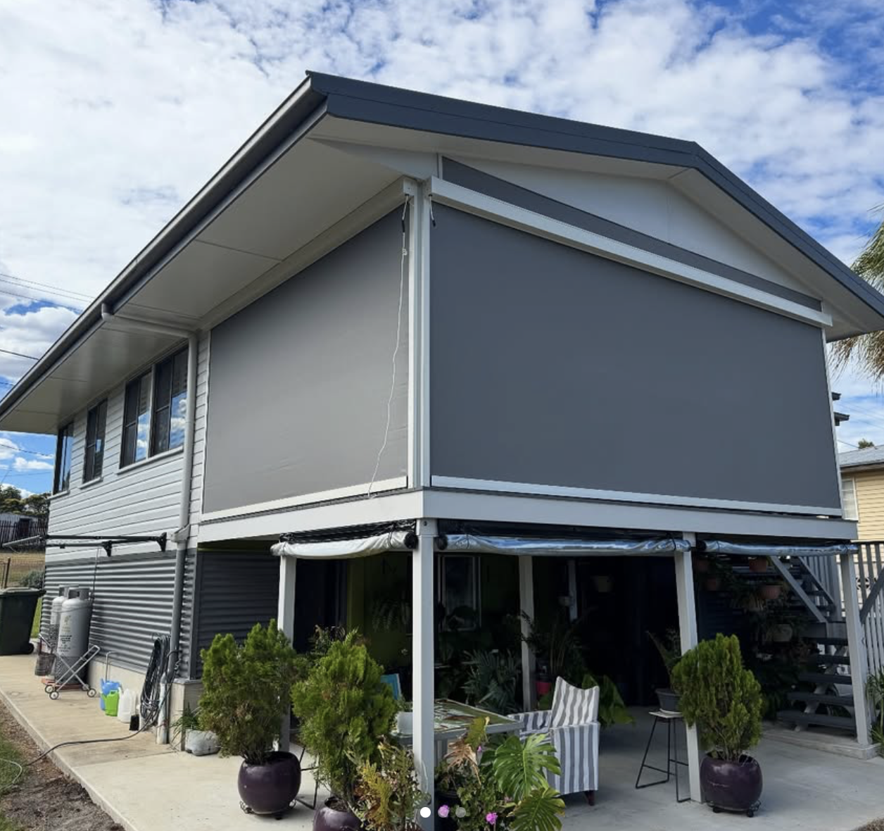 Corner view of the exterior of a house with pitched roof, on stilts with white beams and grey zipscreens
