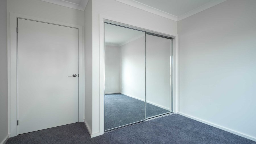 Small bedroom with blue curtains, white walls, white door with black handle, double mirrored wardrobe doors