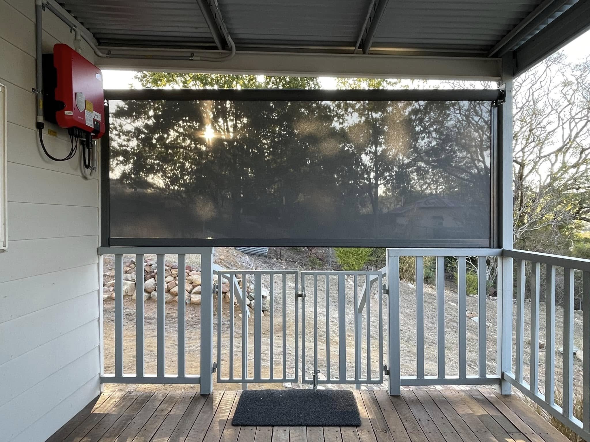 Exterior view of a wooden house with white railings and black external screen blocking the sunlight