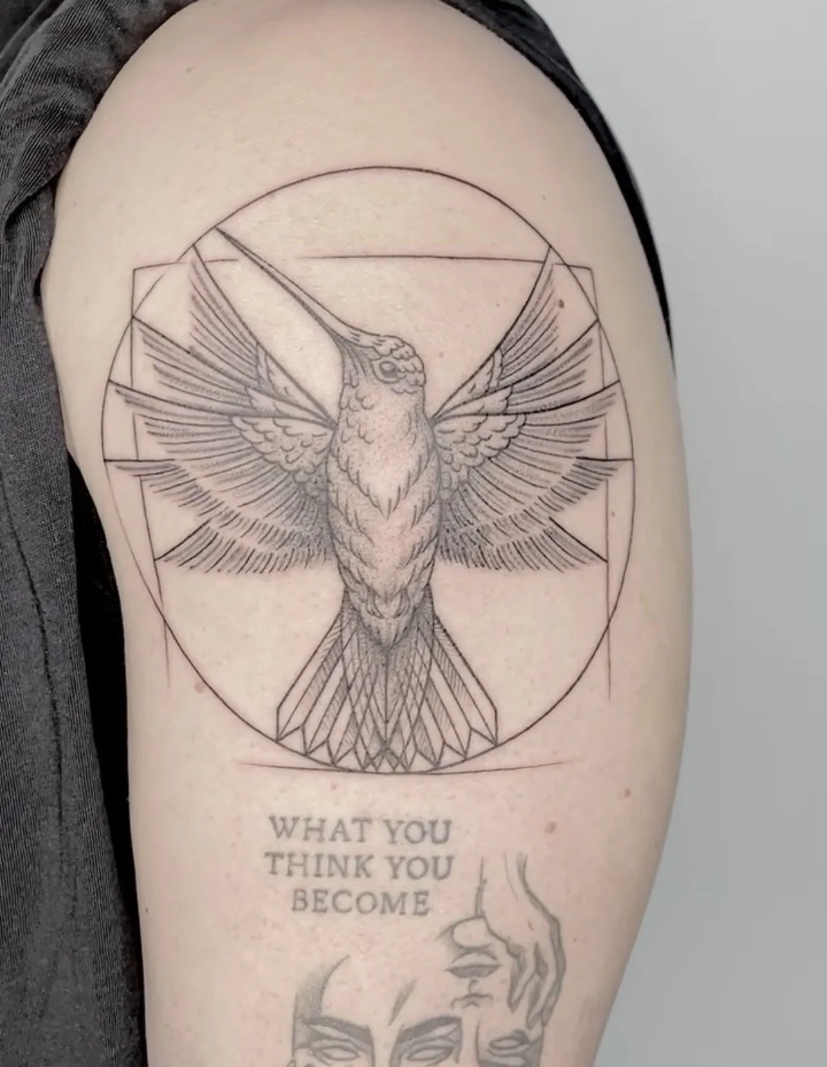 A tattoo of a geometric hummingbird with detailed wings within a circle on a person's upper arm. Below the tattoo, there is text saying "WHAT YOU THINK YOU BECOME" and an outline of a hand.