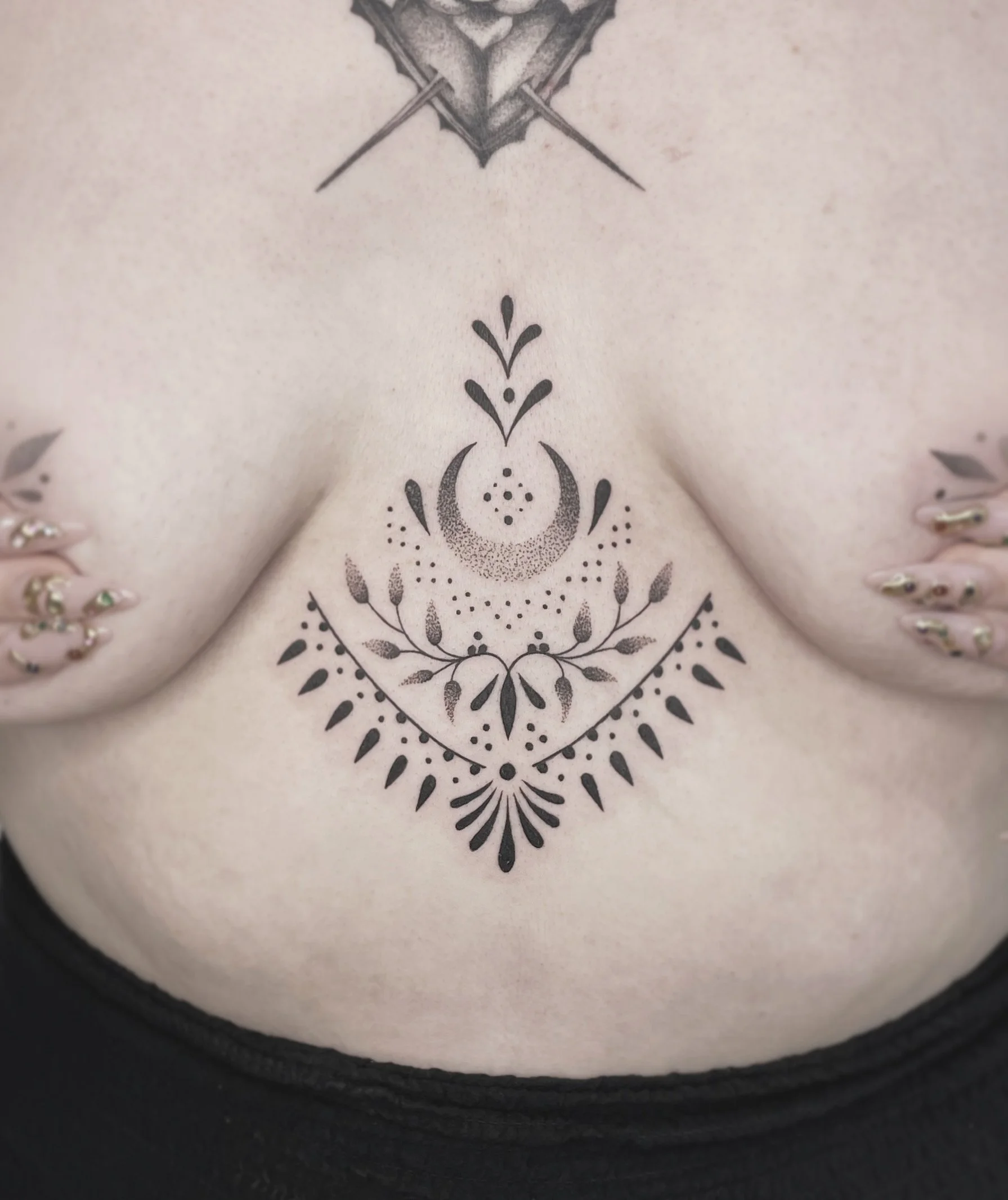 Close-up of a tattoo on a person's skin, showing intricate black ink patterns featuring floral and abstract designs.