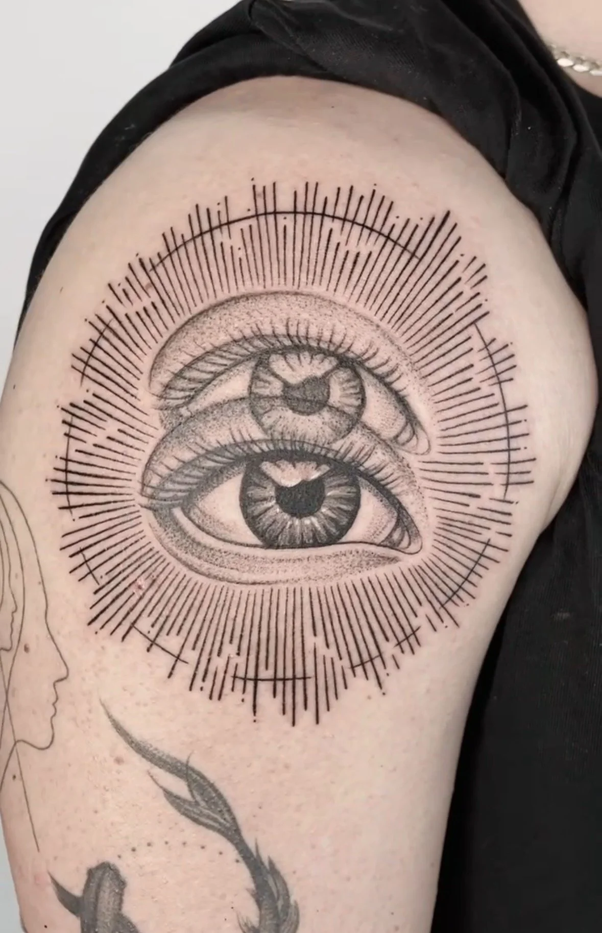 Tattoo of two realistic eyes with detailed irises, surrounded by radiating lines and geometric patterns on the upper arm.