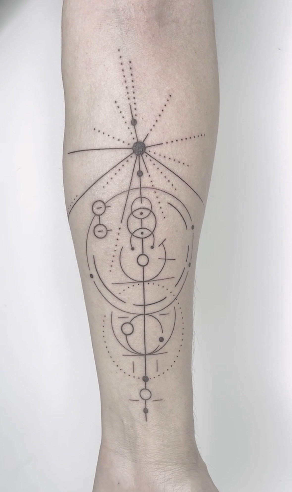 Minimalist geometric tattoo on a person's lower leg, including circles, lines, and dots arranged symmetrically.