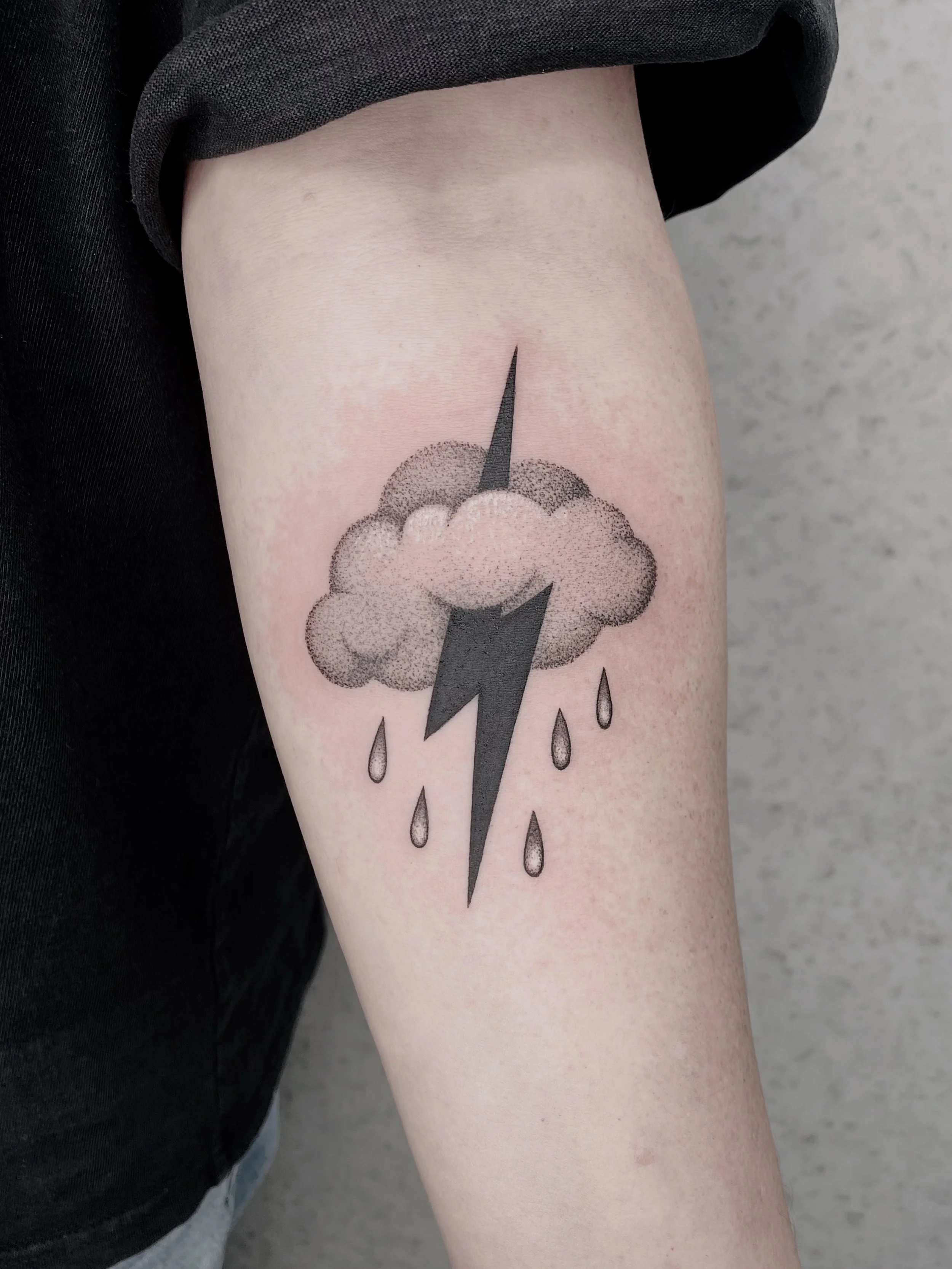A tattoo of a cloud with raindrops and a lightning bolt on a person's upper arm.