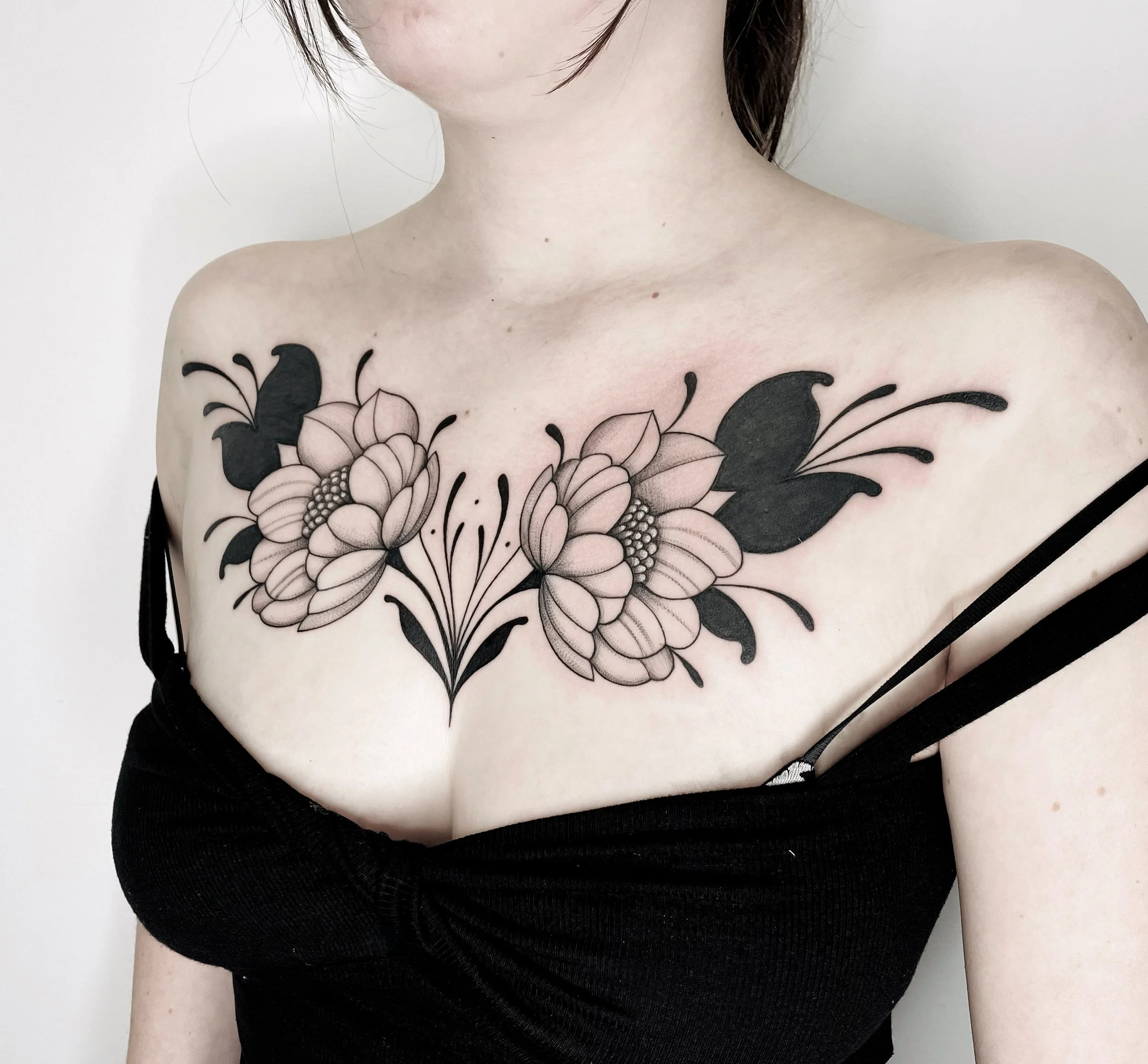 A woman with a floral tattoo on her chest wearing a black top with thin straps.