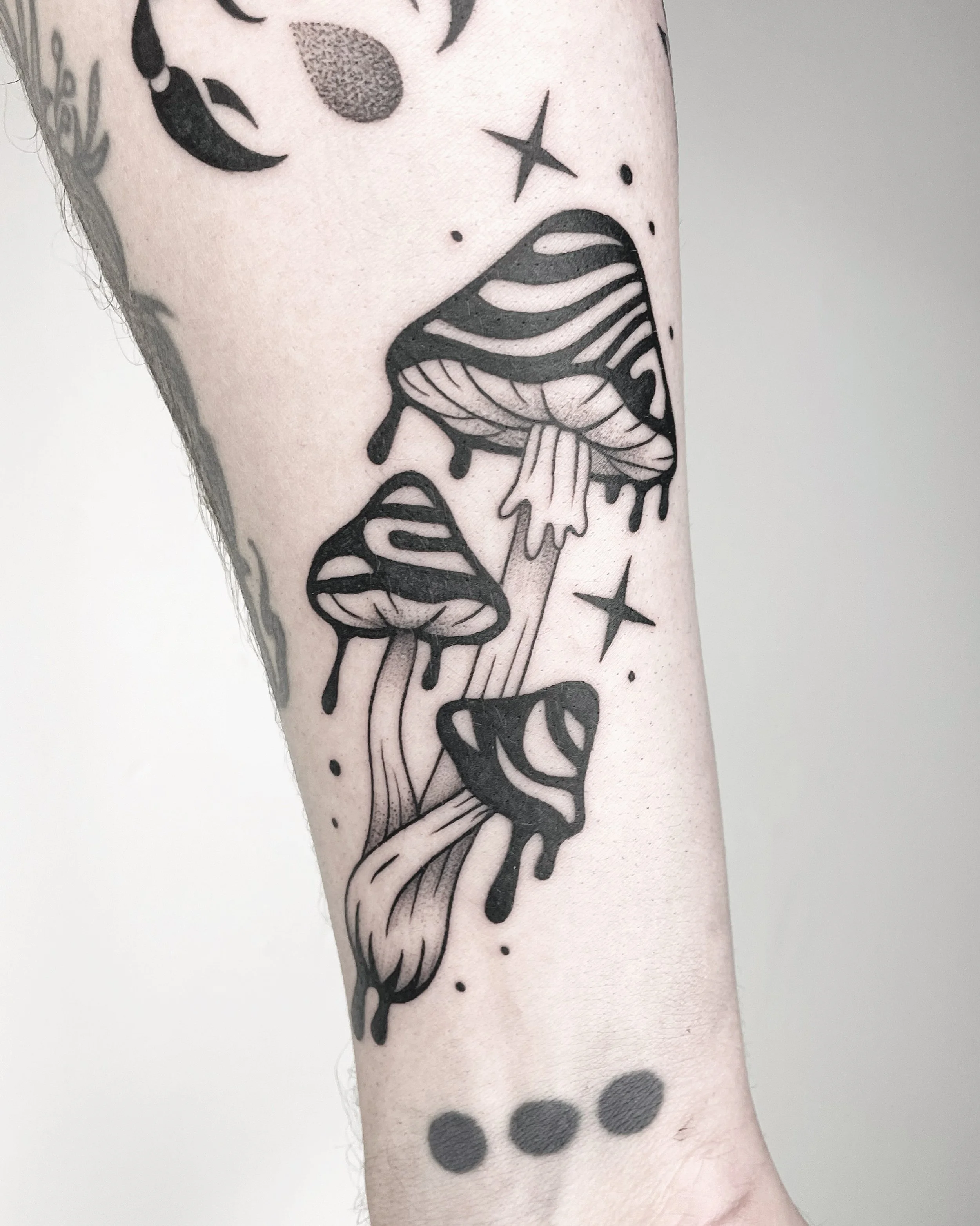 Black line tattoo of a mushroom with dripping paint effect and stars on light skin, with black dot patterns.
