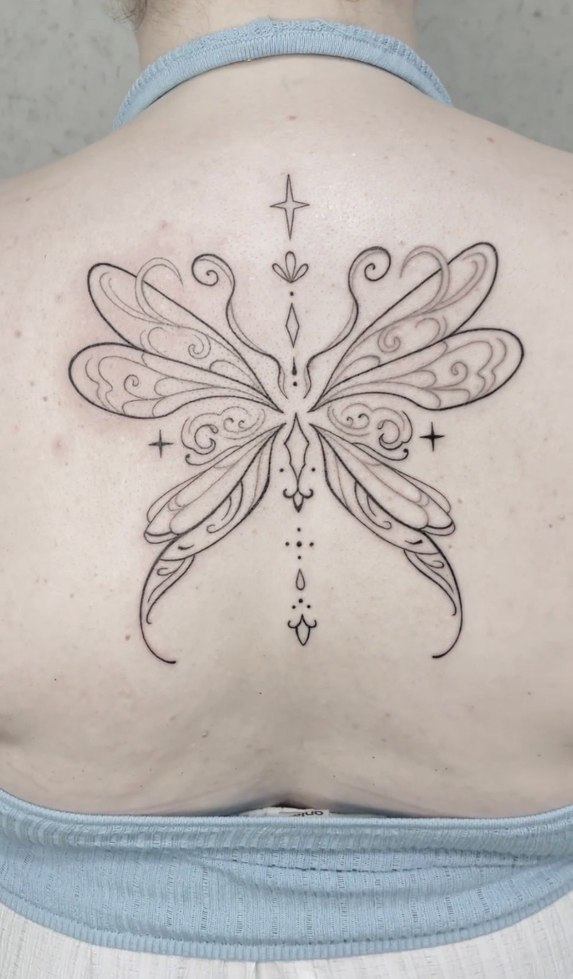 A tattoo of a butterfly with detailed, symmetrical wings and decorative elements on a person's upper back.