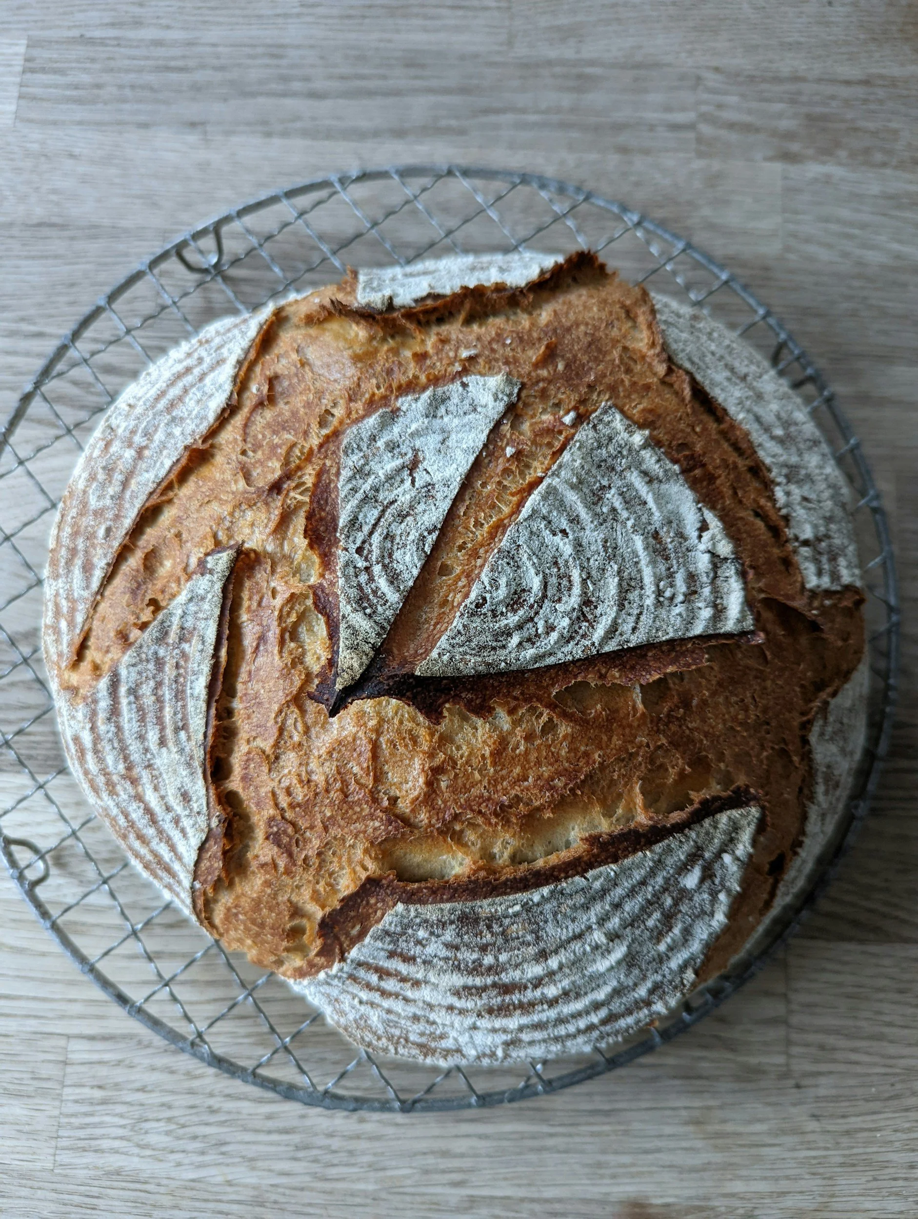Round loaf of artisan sourdough bread with geometric scoring patterns on a cooling rack