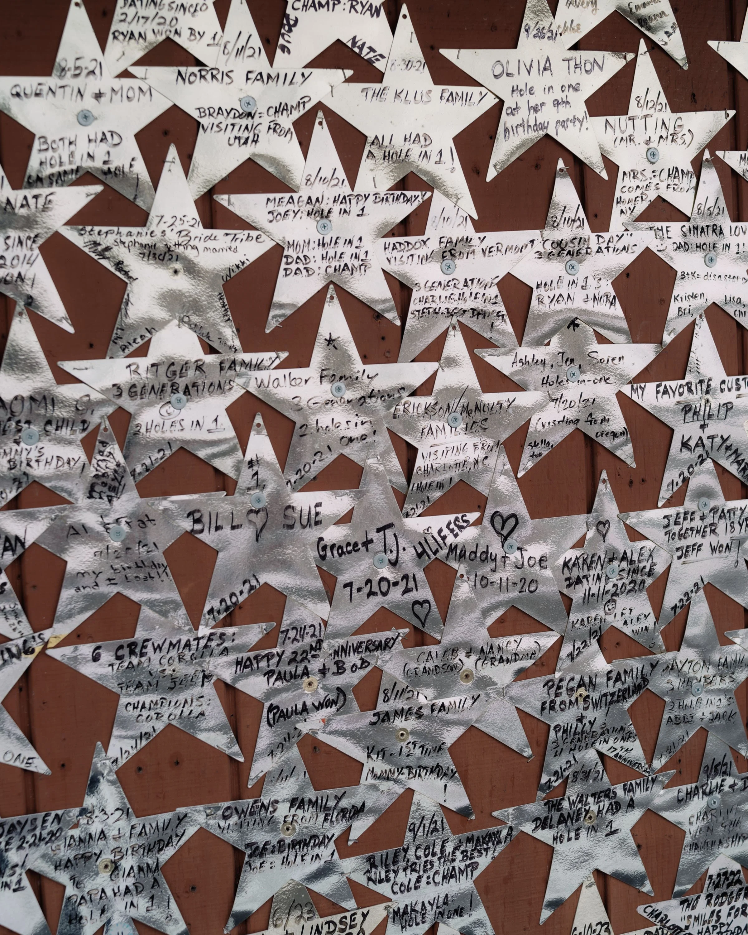 A bulletin board decorated with numerous metallic star-shaped notes with handwritten messages, names, dates, and celebrations for various family members and friends.