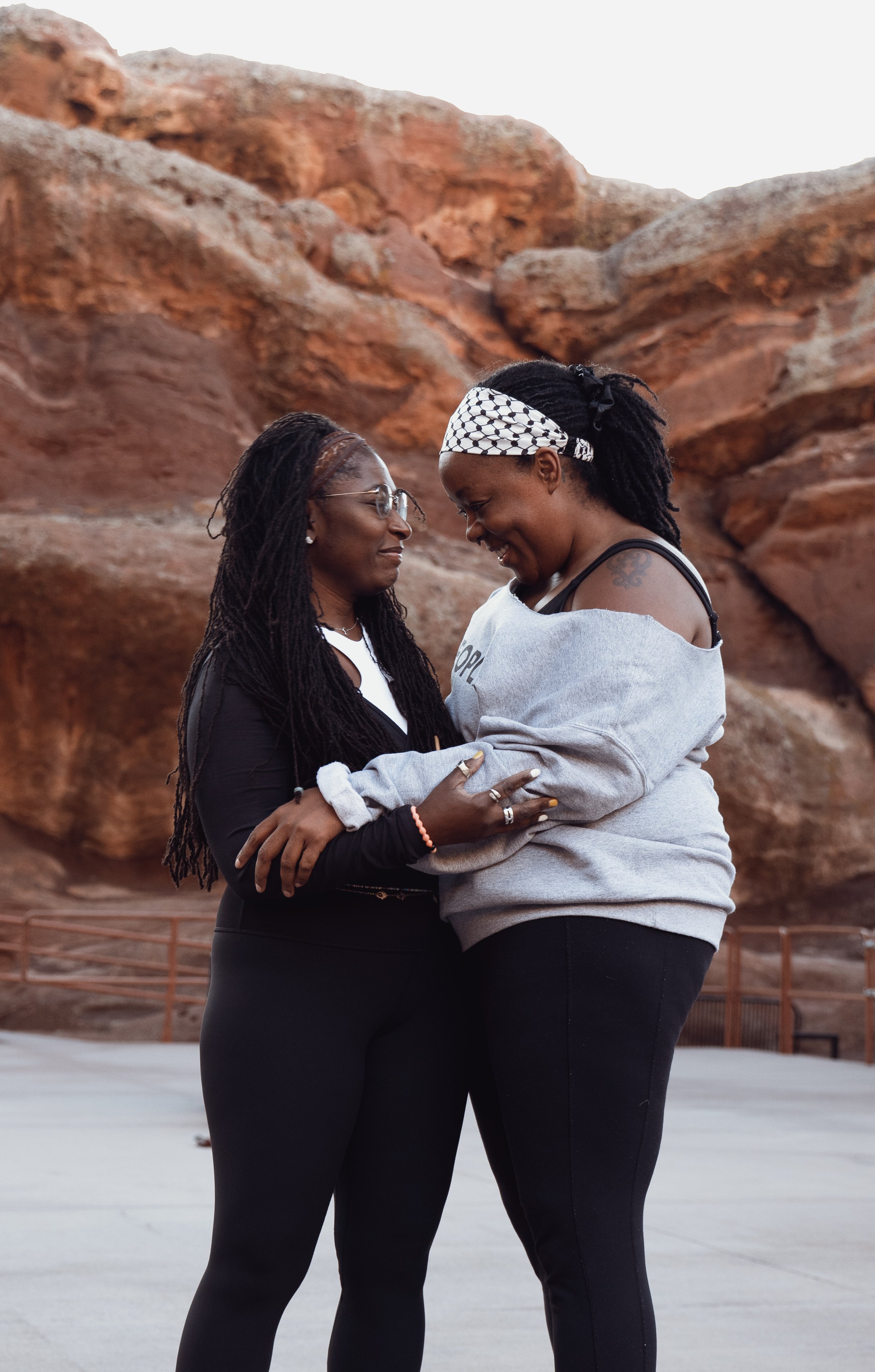 Two women standing close together, smiling, with their foreheads touching, in front of rocky landscape.