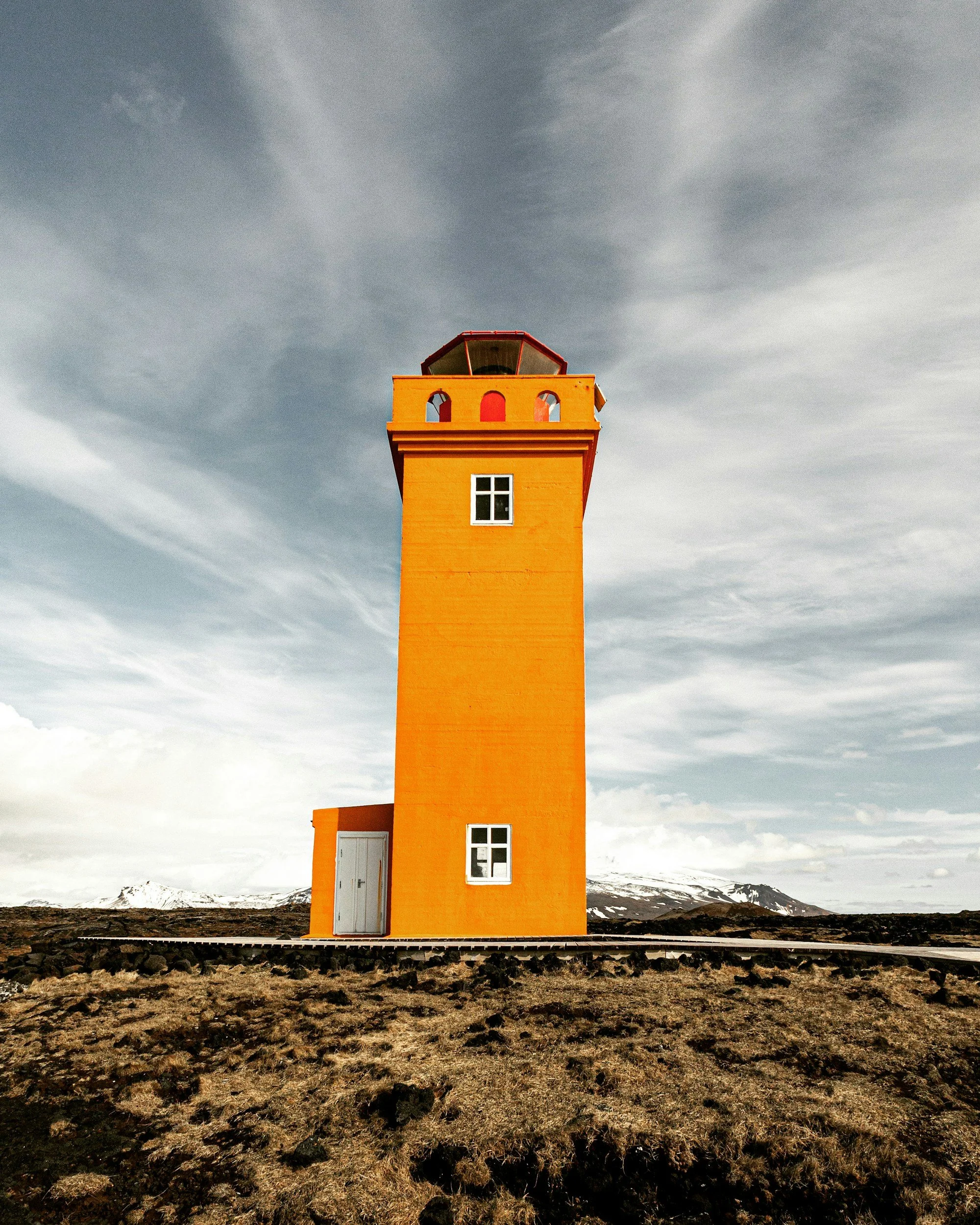 Orange lighthouse against a cloudy sky in a barren landscape
