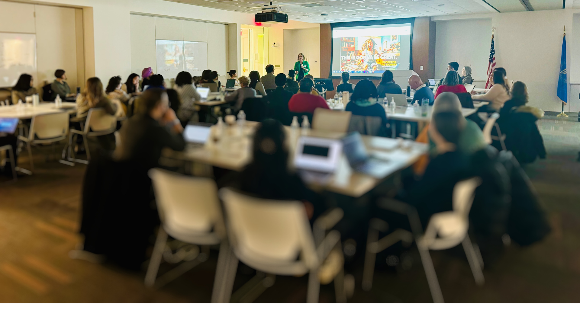 People attending a presentation on burnout recovery in a conference room with a projector screen and laptops on tables.