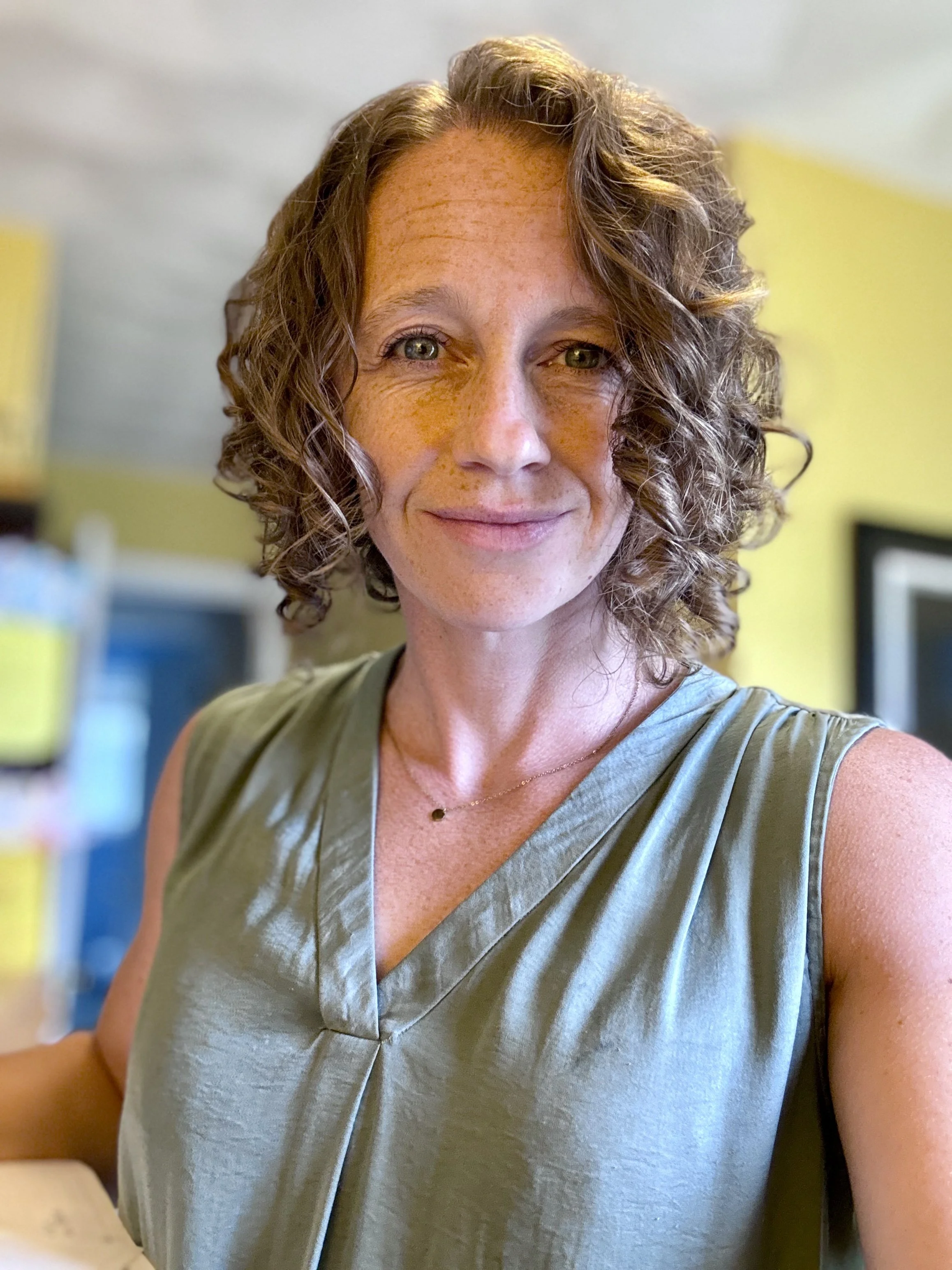 Burnout recovery coach with curly hair smiling indoors, wearing a green top