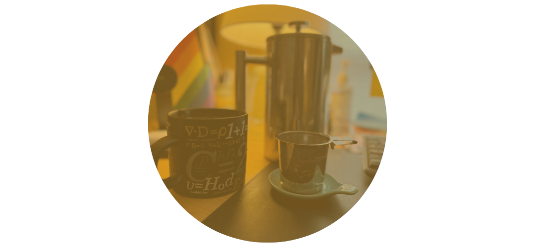 Coffee mug with scientific equations, French press, and tea infuser on a desk.
