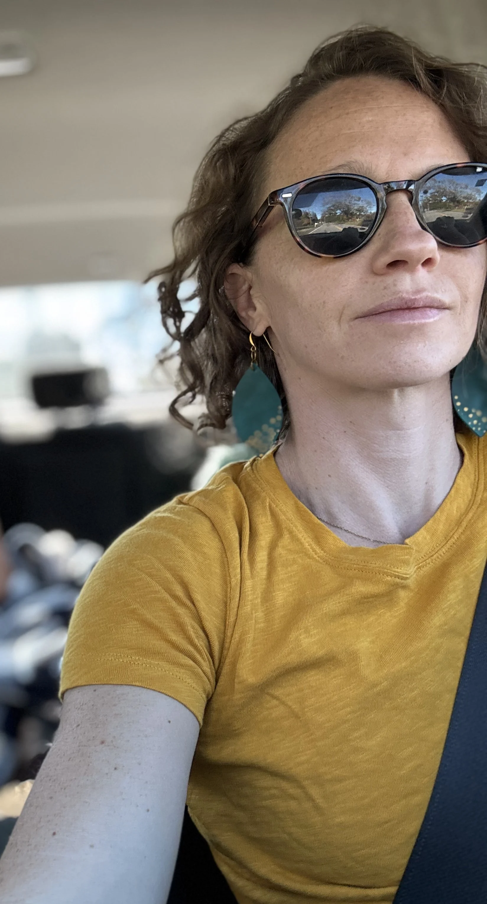 Burnout recovery coach, a woman, wearing sunglasses and a yellow shirt driving