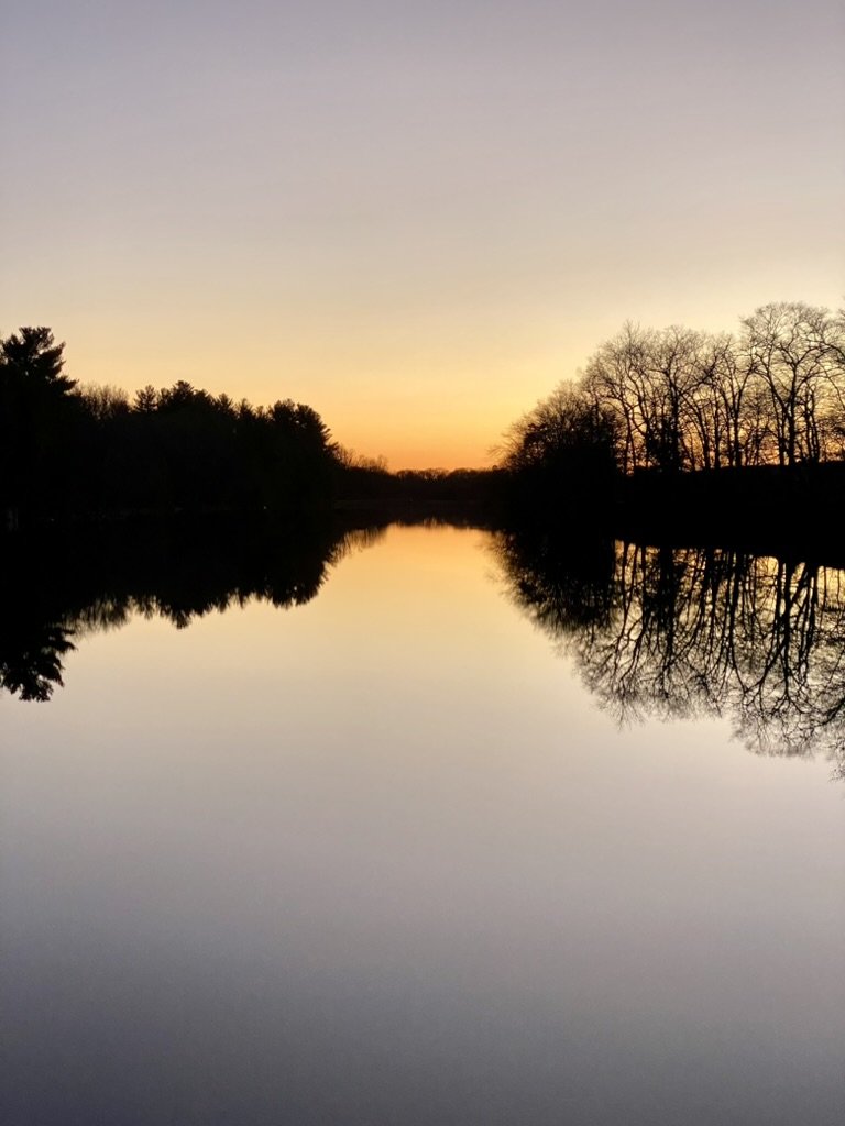 Sunset over a calm river with trees reflecting on the water.