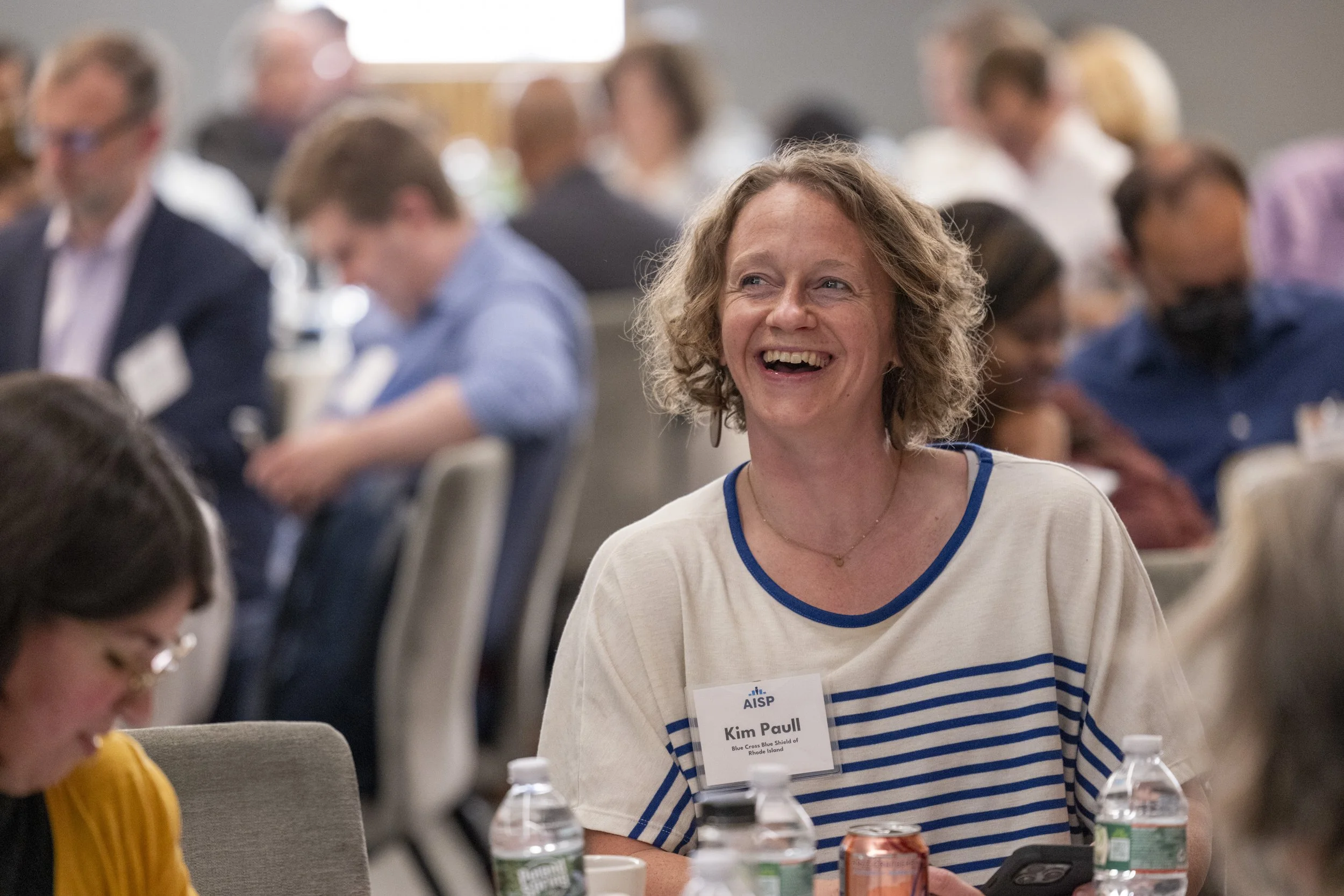 Burnout recovery coach laughing at a conference with people in the background.
